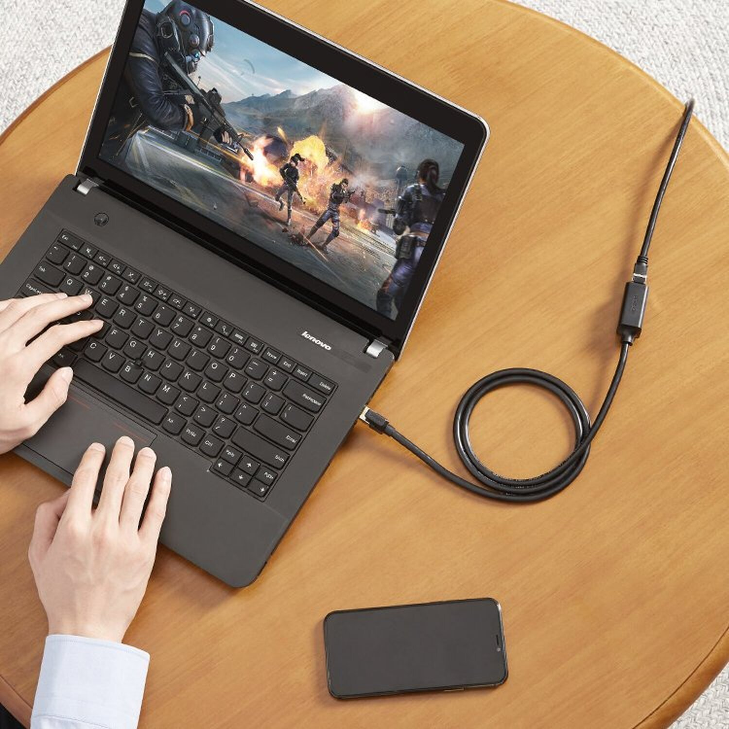 Ein Laptop ist mit einem Kabel verbunden. Ein Telefon liegt auf dem Tisch.