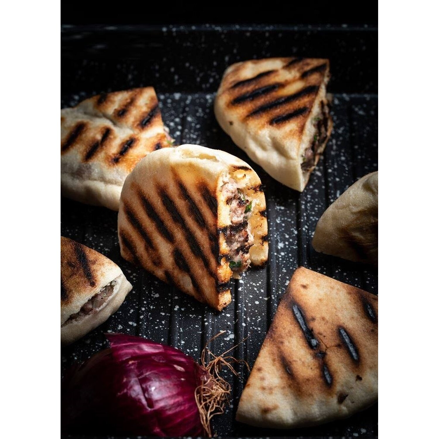 Gegrillte Fladenbrot-Sandwiches, aufgeschnitten, Füllung zeigend. Rote Zwiebel auf dem Grill.
