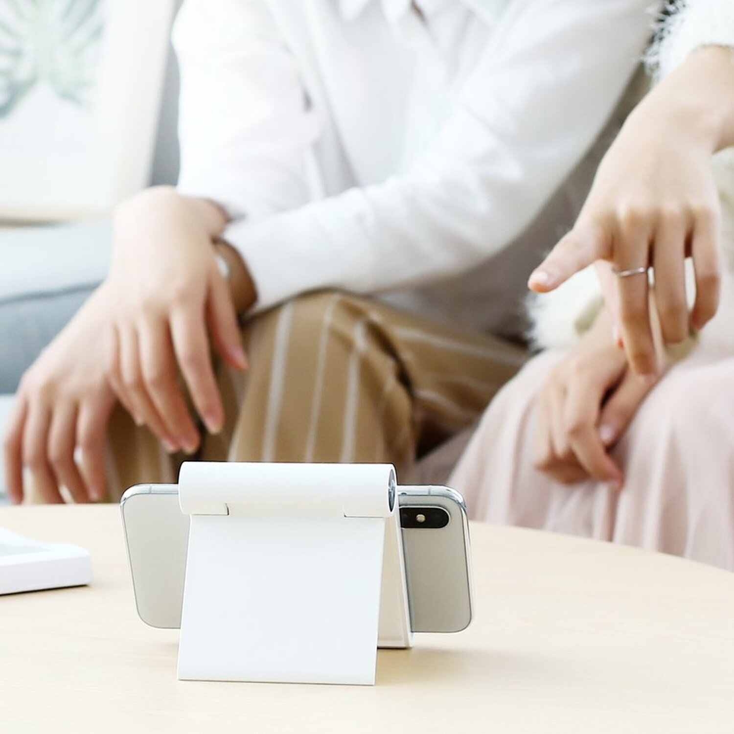 Dwie osoby w pobliżu stojaka na telefon trzymające dwa telefony, na stole.