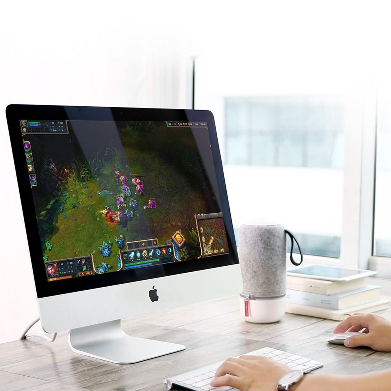 iMac z grą na ekranie, głośnikiem i ręką osoby.