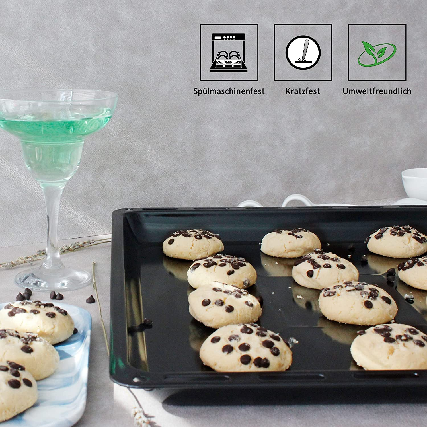 Cookies mit Schokostückchen auf einem Backblech, ein Cocktail und Symbole auf grauem Hintergrund.