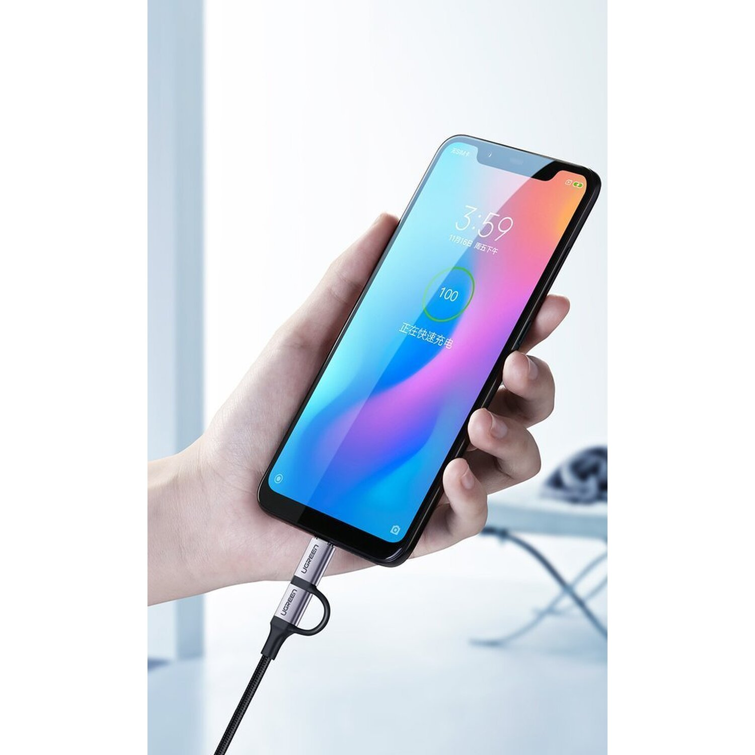 Telefon ładujący się kablem. Pokazuje 100% baterii i godzinę. Ręka trzyma telefon.