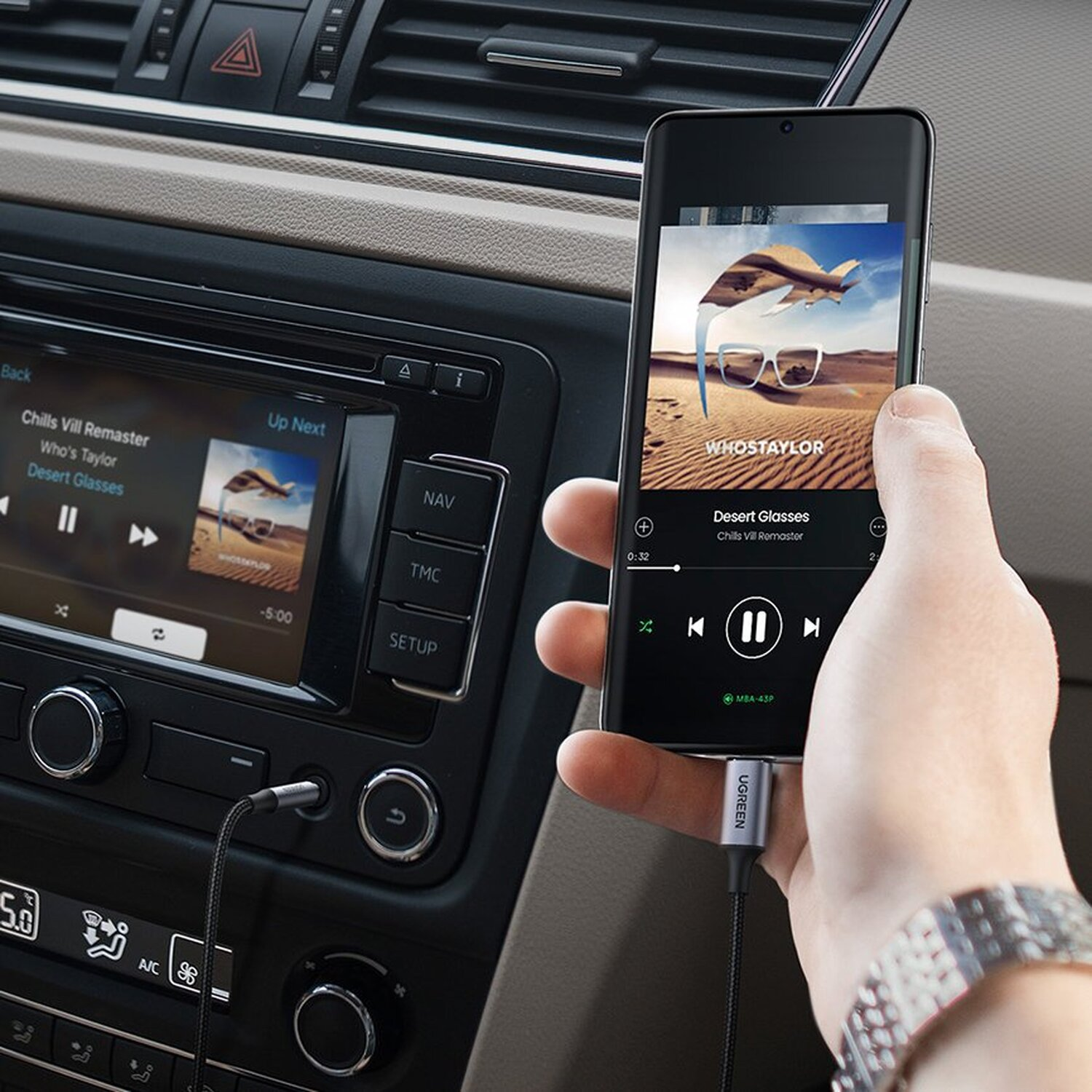 Ręka trzyma telefon w samochodzie, podłączony do gniazda audio.