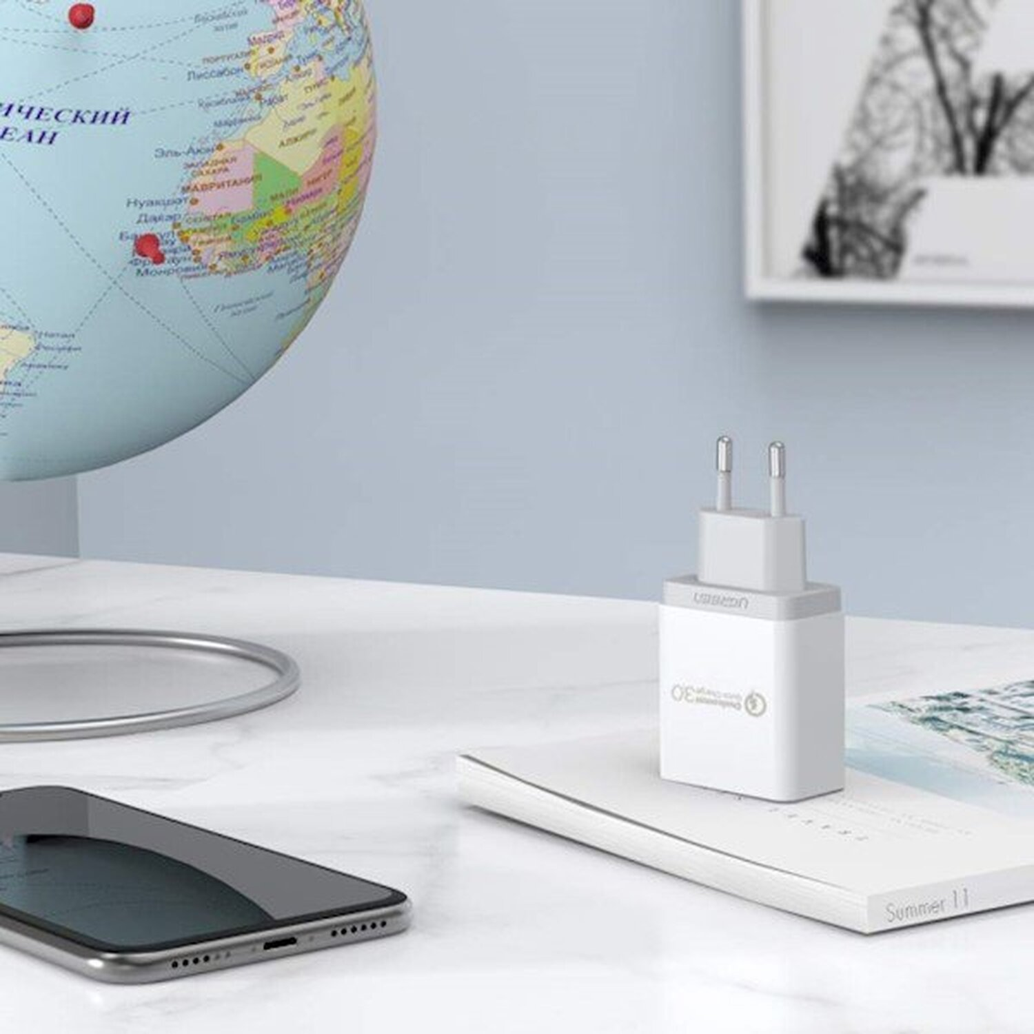 Biała ładowarka na białej powierzchni z książką i telefonem. Globus w tle.