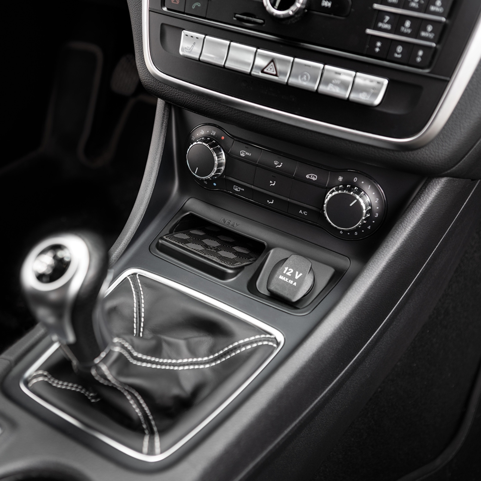 Autointerieur, zeigt Schalthebel, Luftauslässe und eine 12-V-Steckdose. Schwarz-Silber-Akzente.