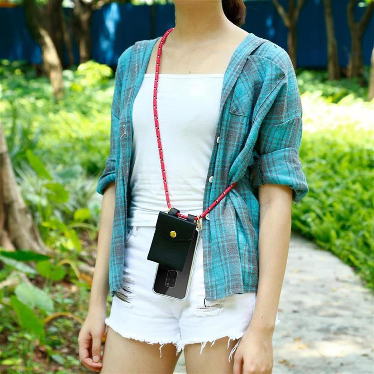 Donna con custodia per telefono con portafoglio nero, carte e corda rossa. All'aperto con pantaloncini bianchi e camicia blu.