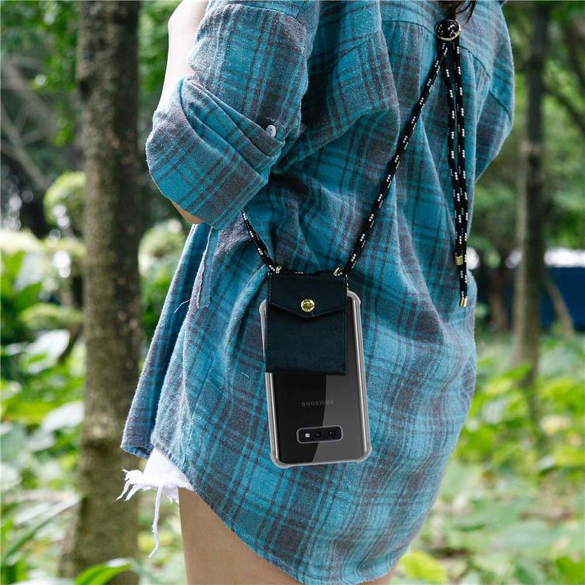 Una persona con una camicia a quadri blu tiene in mano un telefono in una custodia nera con una cinghia a corda nera.