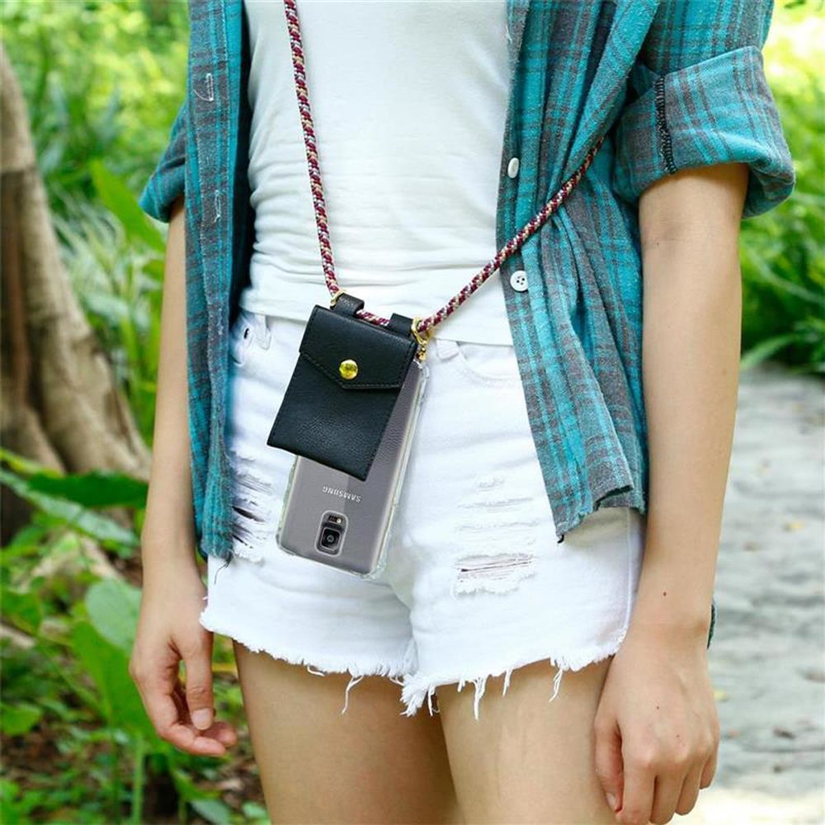 Una persona che indossa un cordino tiene un telefono in una custodia. La persona indossa una camicia a quadri e pantaloncini.