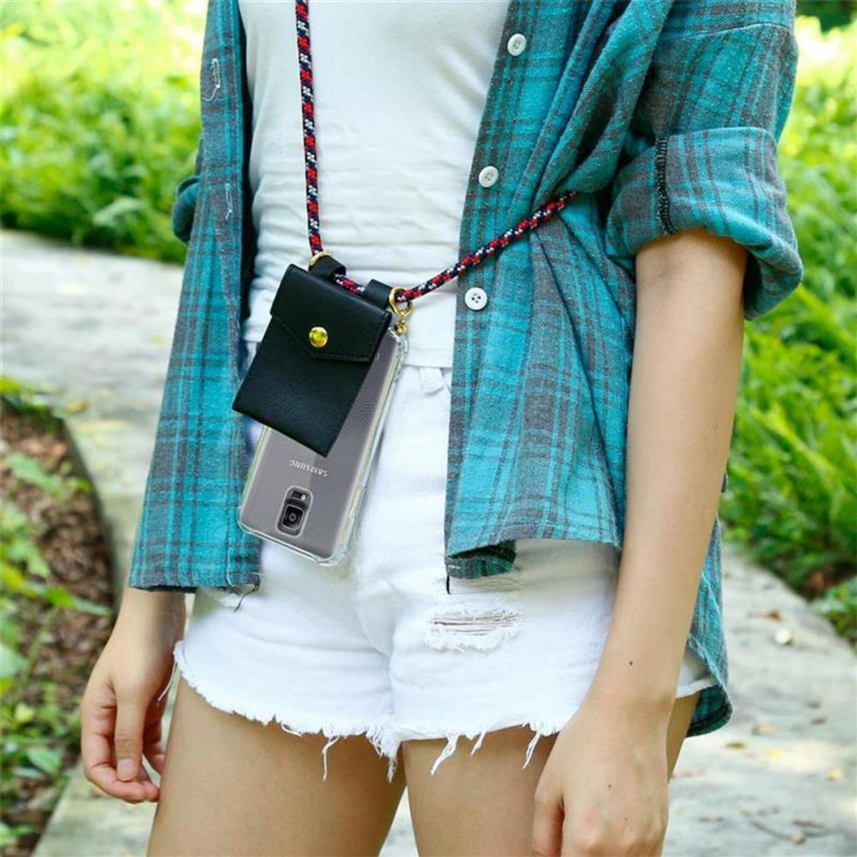 Una donna che indossa una camicia a quadri verde acqua e pantaloncini bianchi ha una custodia per telefono con un cordino.