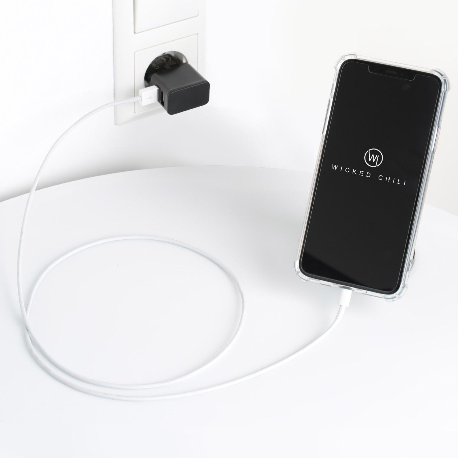 Telefon wird auf einem weißen Tisch geladen. Ladegerät in der Steckdose, Telefon auf Ständer. Weißes Kabel verbindet.