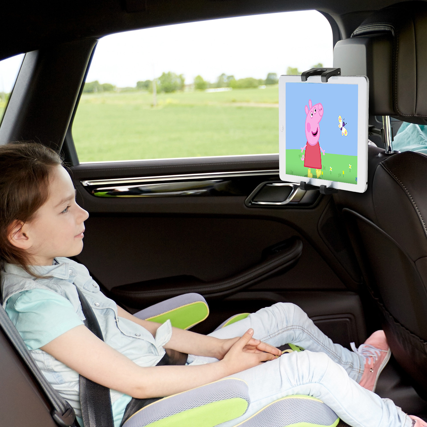 Ein Mädchen im Auto schaut sich einen Tablet mit Peppa Wutz an. Das Tablet ist am Kopfstützen.