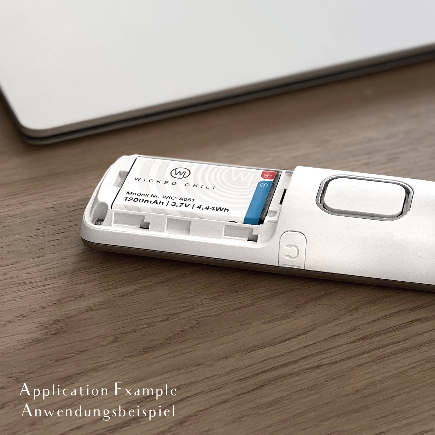 Weißes elektronisches Gerät mit Batterie, auf einem Holztisch, mit deutschem Text.