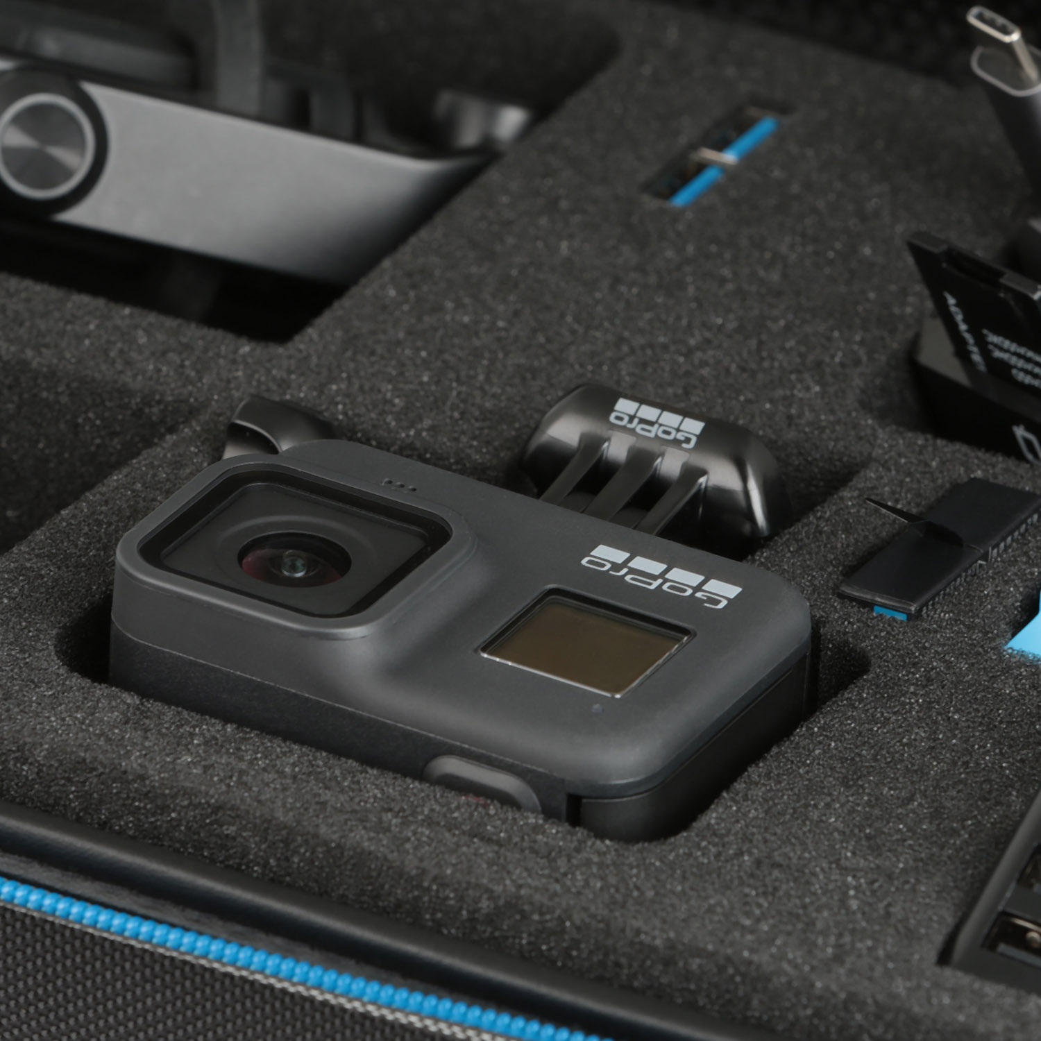 GoPro-Kamera und Zubehör in einem Koffer. Die Kamera ist schwarz. Schaumstoffpolsterung innen. Verschiedene kleine Gegenstände.
