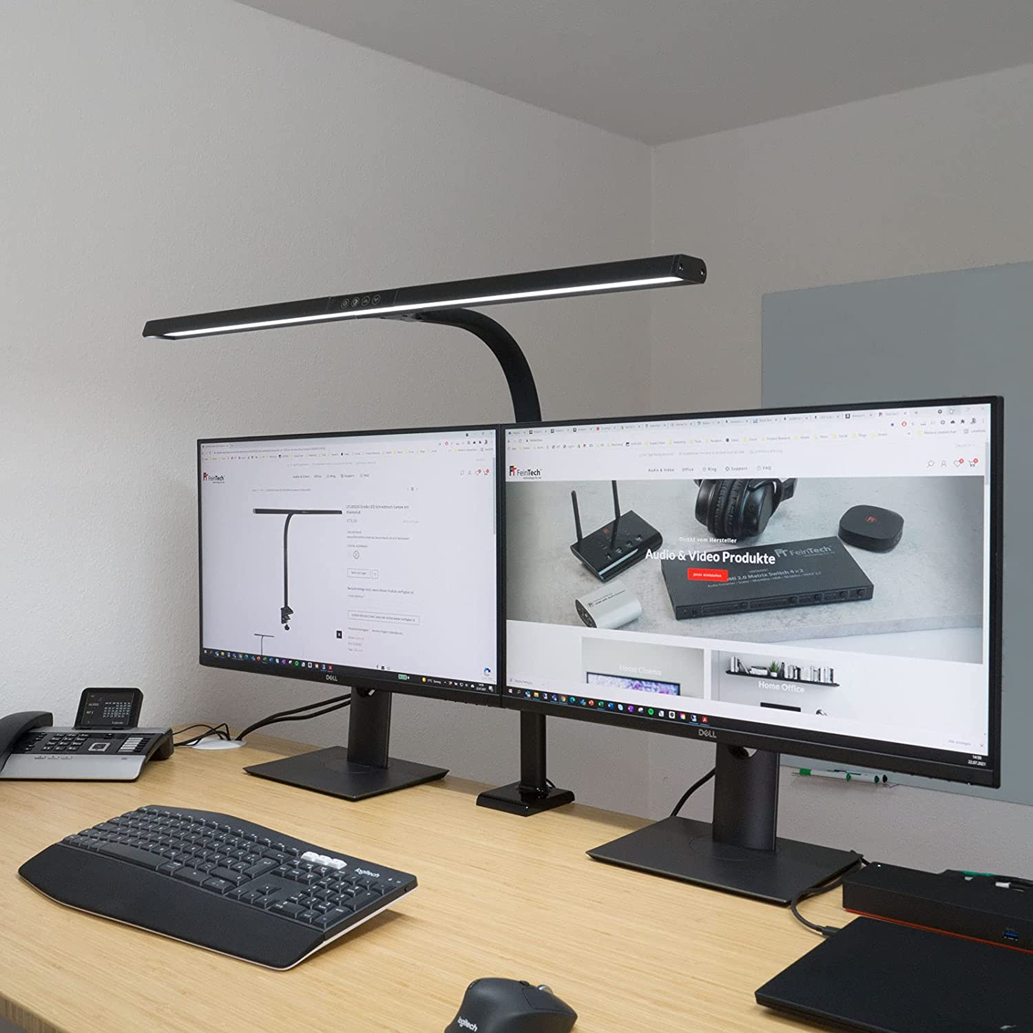 Schreibtisch mit zwei Monitoren und einer Schreibtischlampe. Tastatur, Maus und Telefon sind sichtbar.