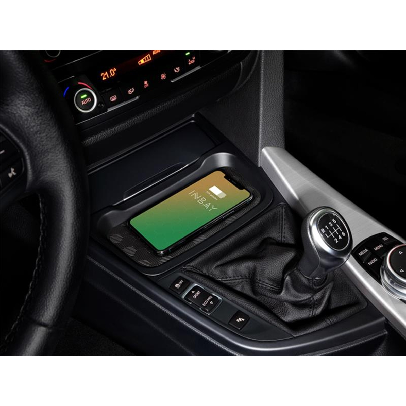Ein Auto-Innenraum mit einem kabellos ladenden Telefon in einer Ablage. Der Schalthebel ist sichtbar.