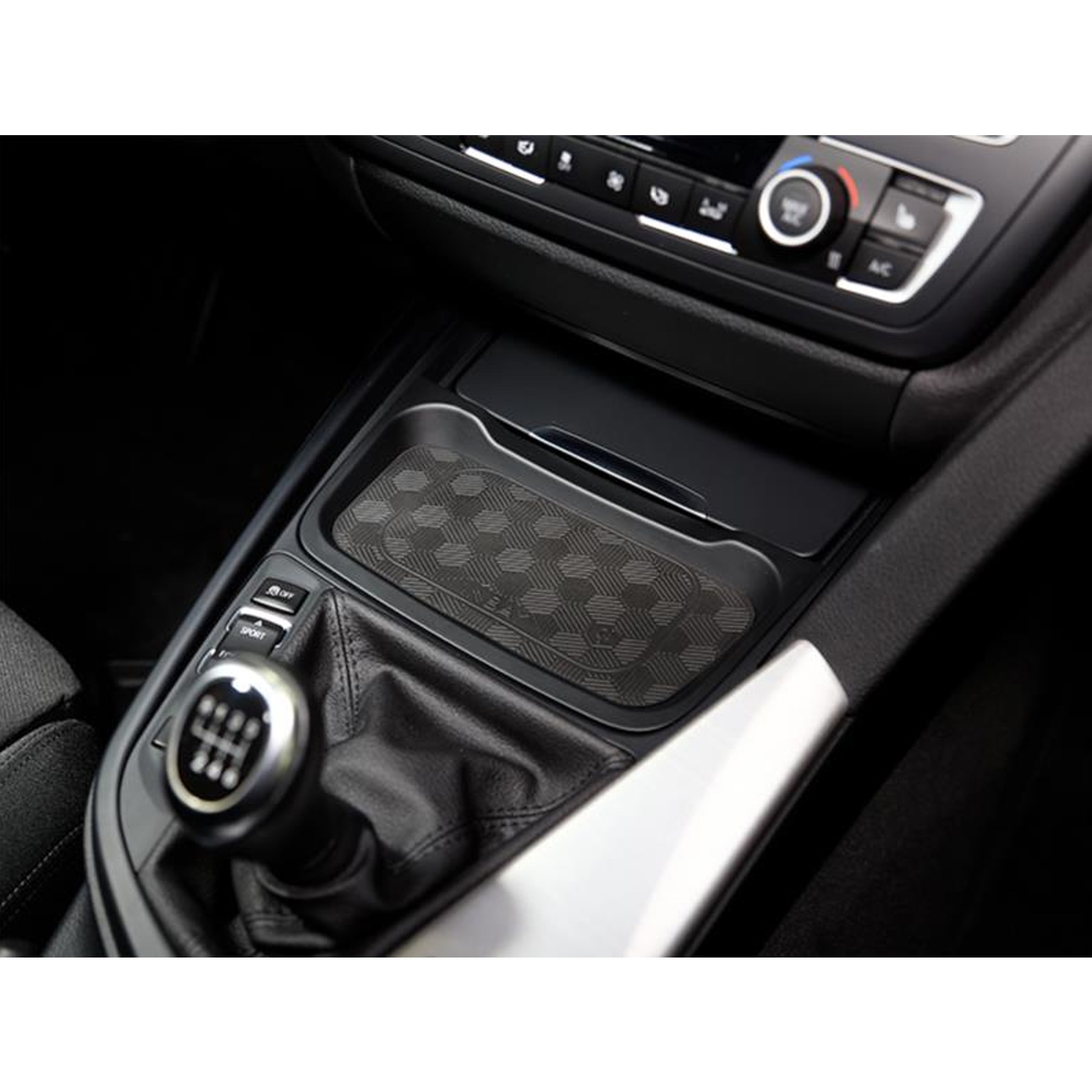 Auto-Innenraum mit Schalthebel, Konsole und Fach mit gemusterter Matte.
