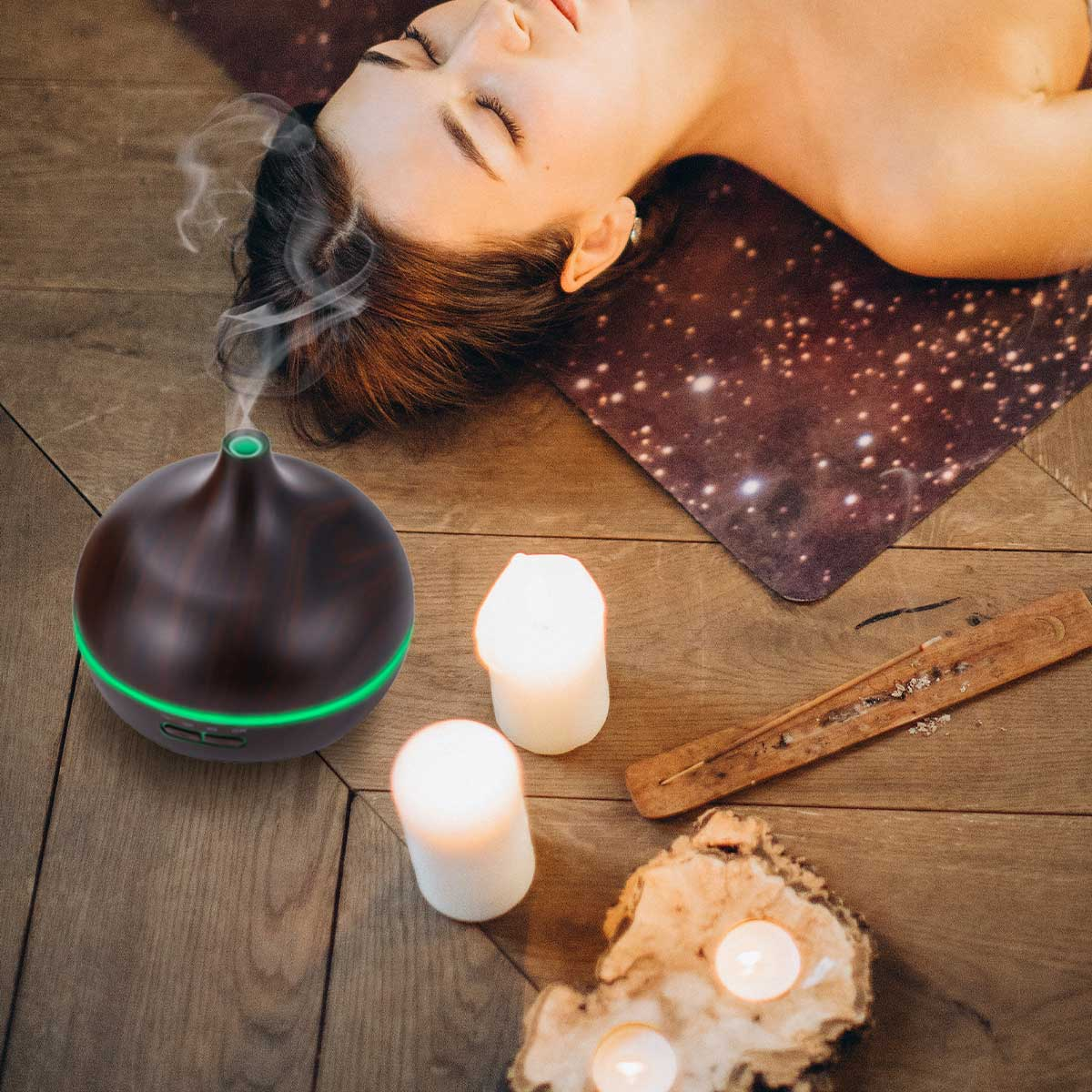 Kobieta leżąca z dyfuzorem, świecami, kadzidłem i drewnem na drewnianej podłodze.