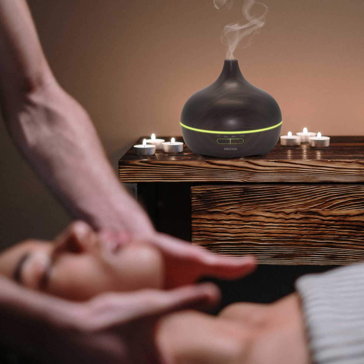 Dyfuzor zapachów na drewnianym stole ze świecami. Osoba wykonuje masaż.