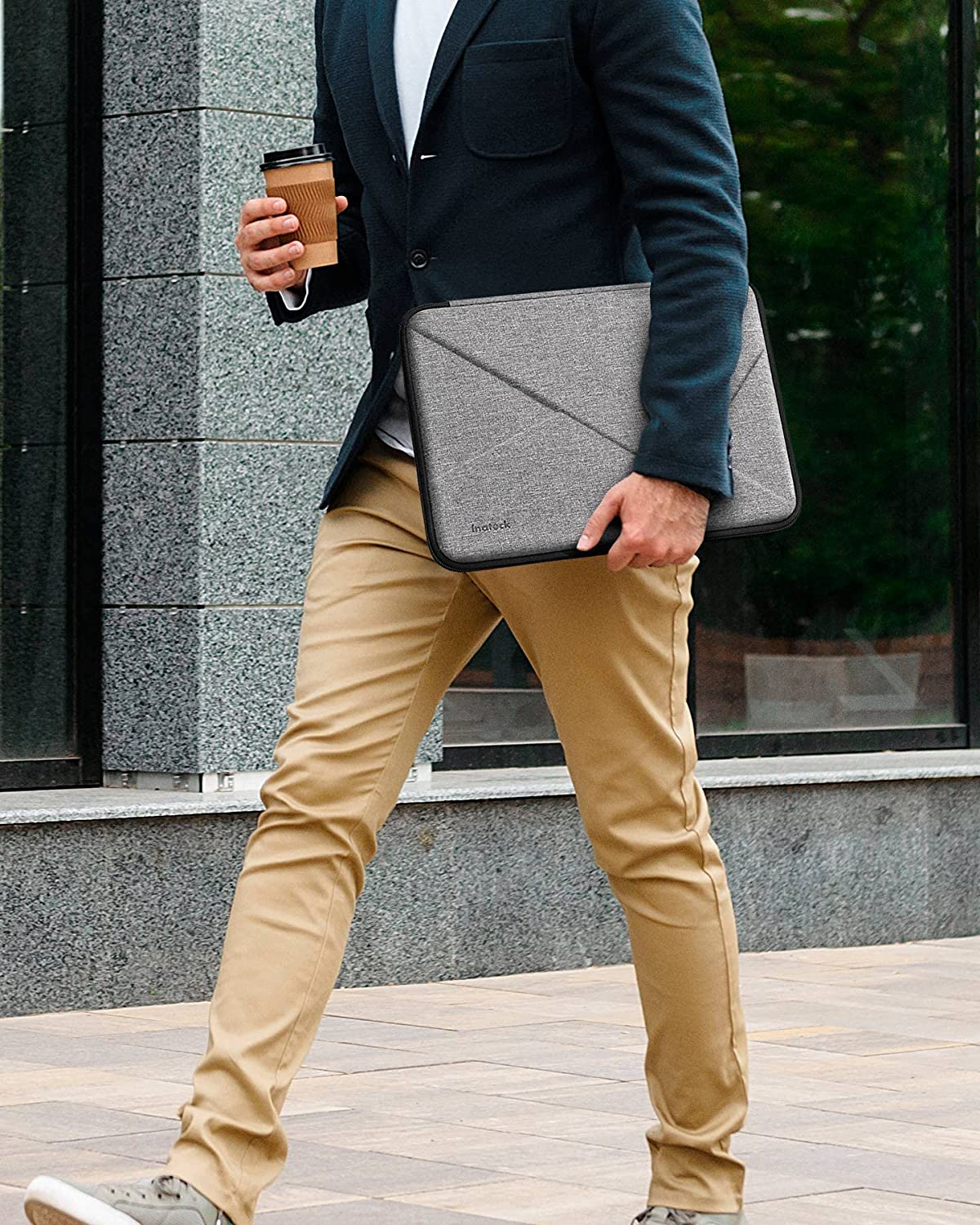 Ein Mann im Anzug geht mit einer Laptoptasche. Er trägt eine Kaffeetasse.