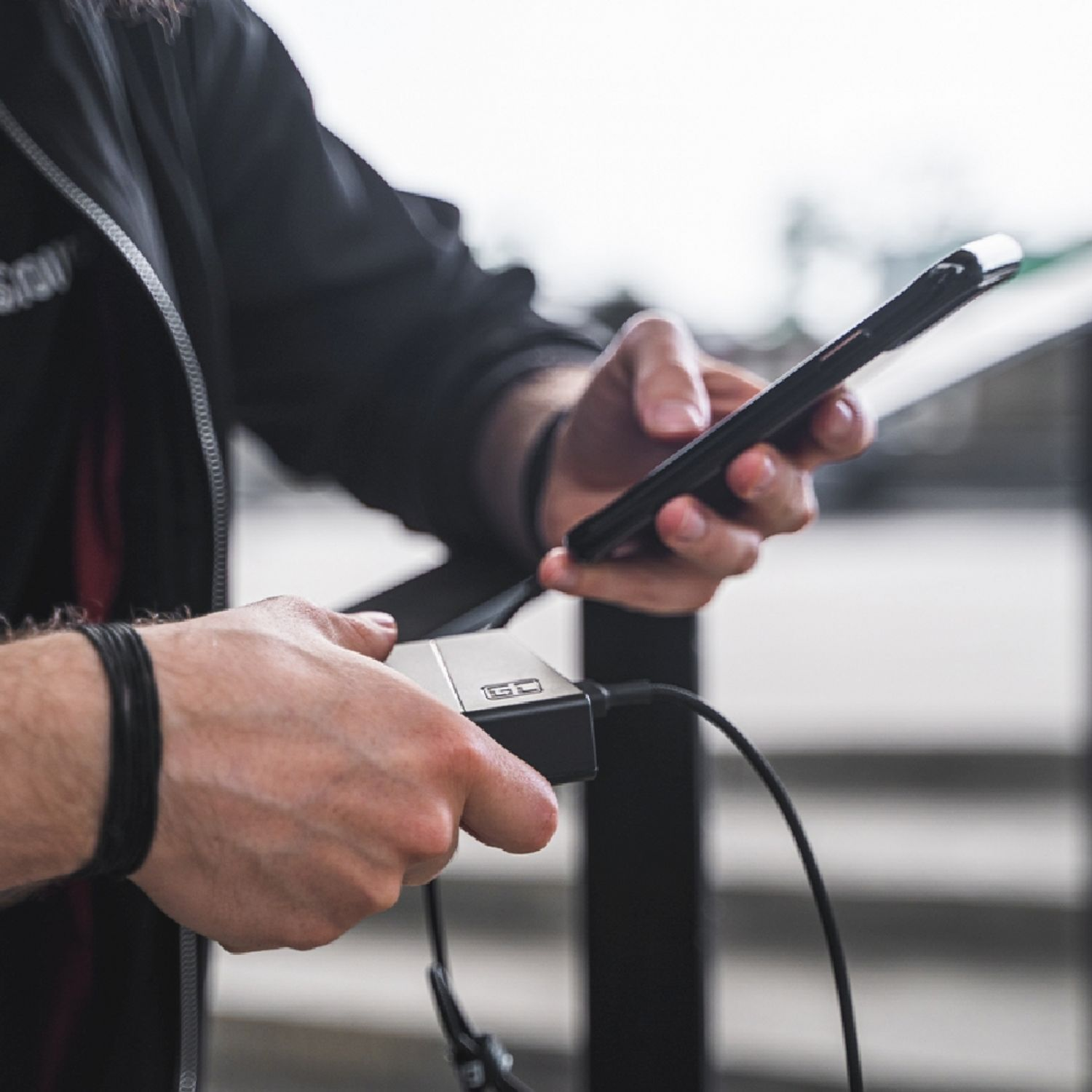 Person hält ein Telefon und eine Powerbank, verbunden mit einem schwarzen Kabel.