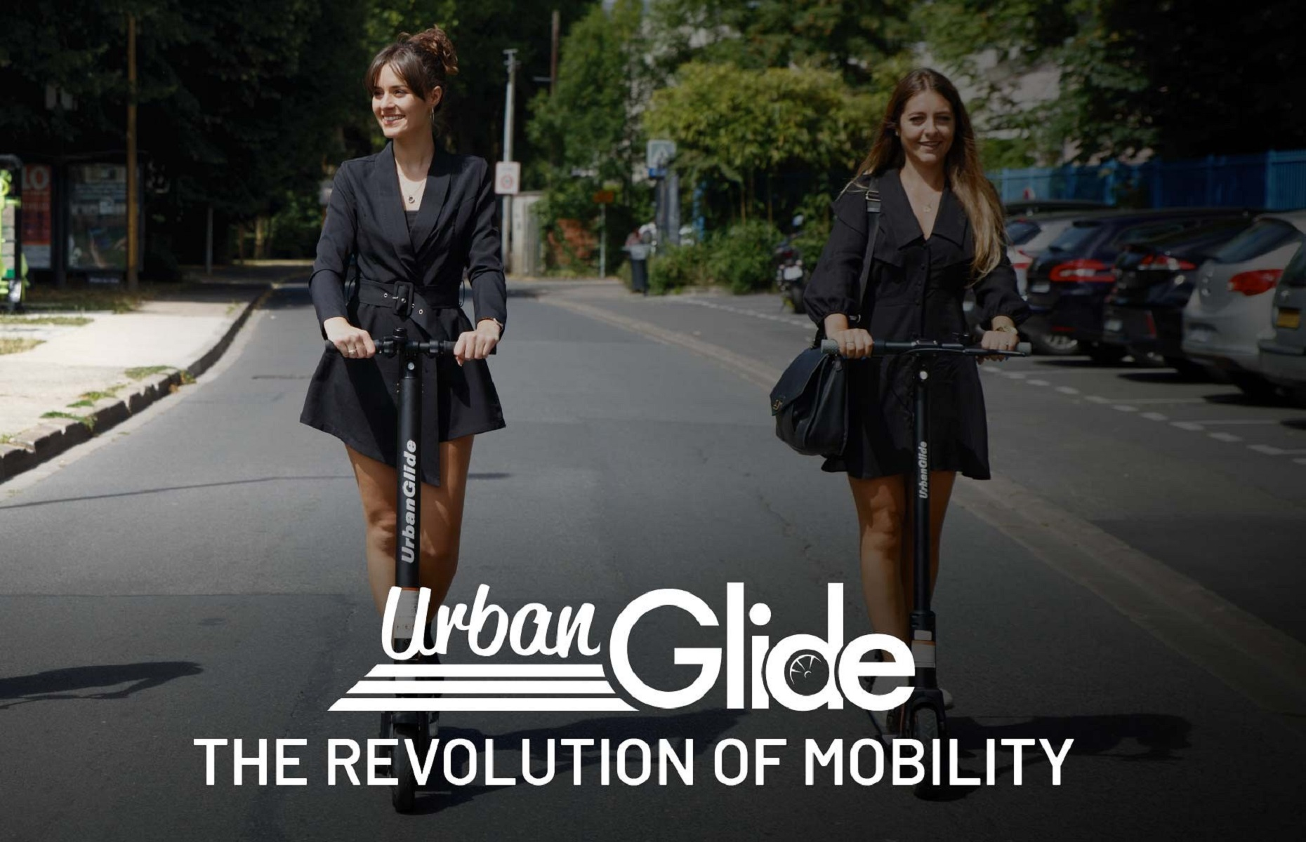 Dos mujeres en patinetes en una carretera. El logo 'Urban Glide' aparece en el patinete y debajo.