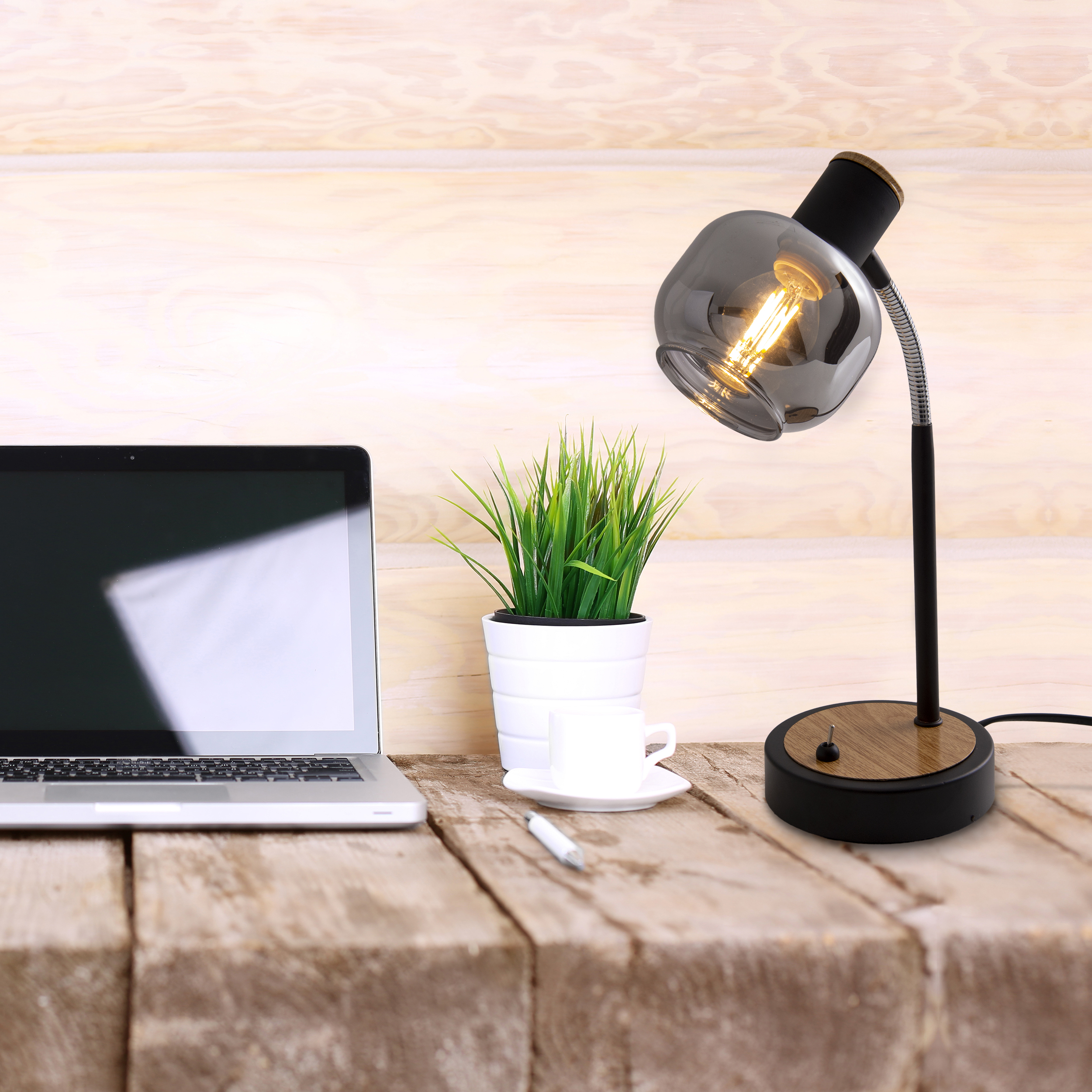 Scrivania con laptop, lampada, pianta e tazza di caffè. Superficie in legno.