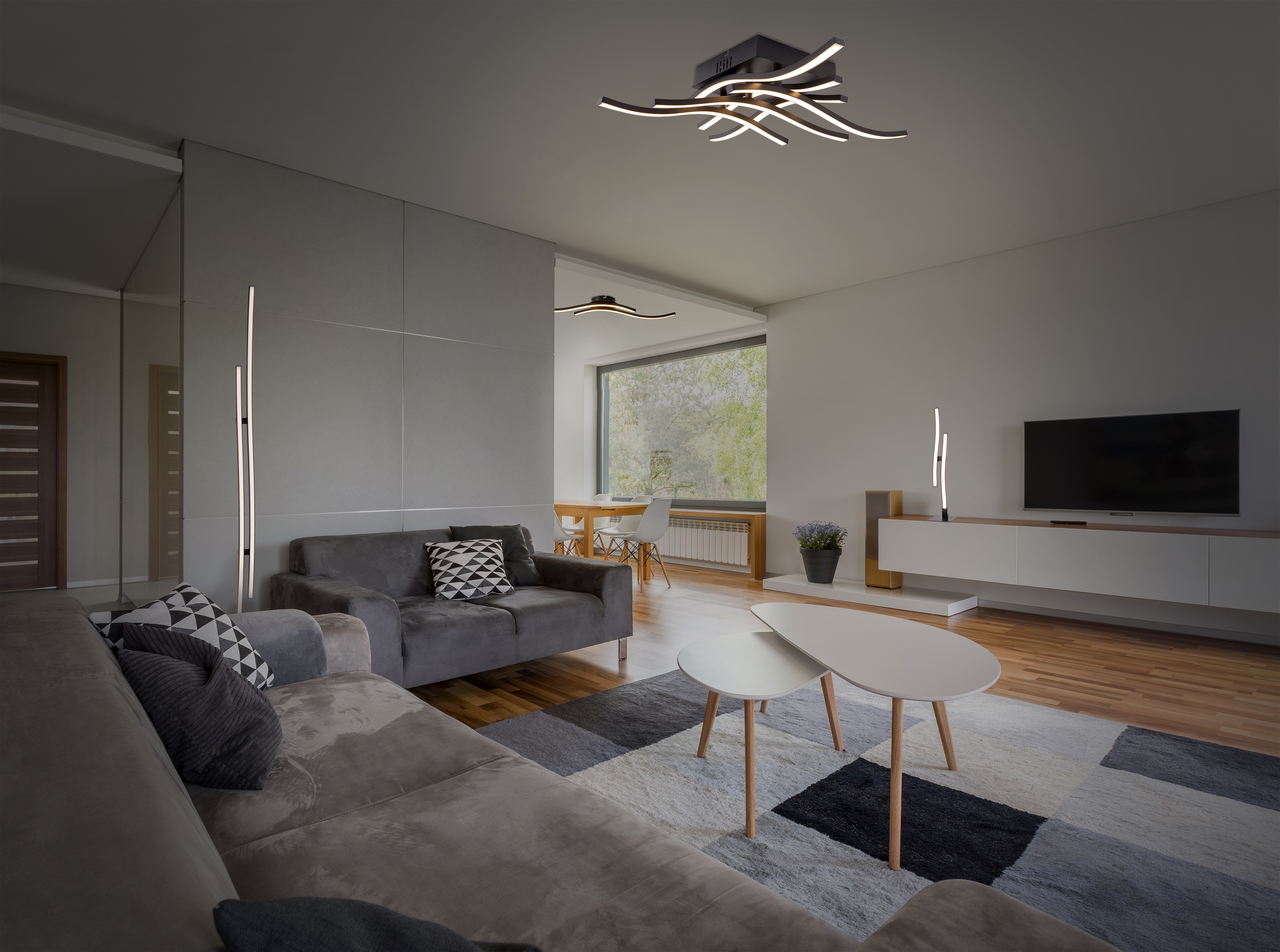 Modernes Wohnzimmer mit grauem Sofa, Teppich und Lichtern. Weiße Wände und Holzboden.