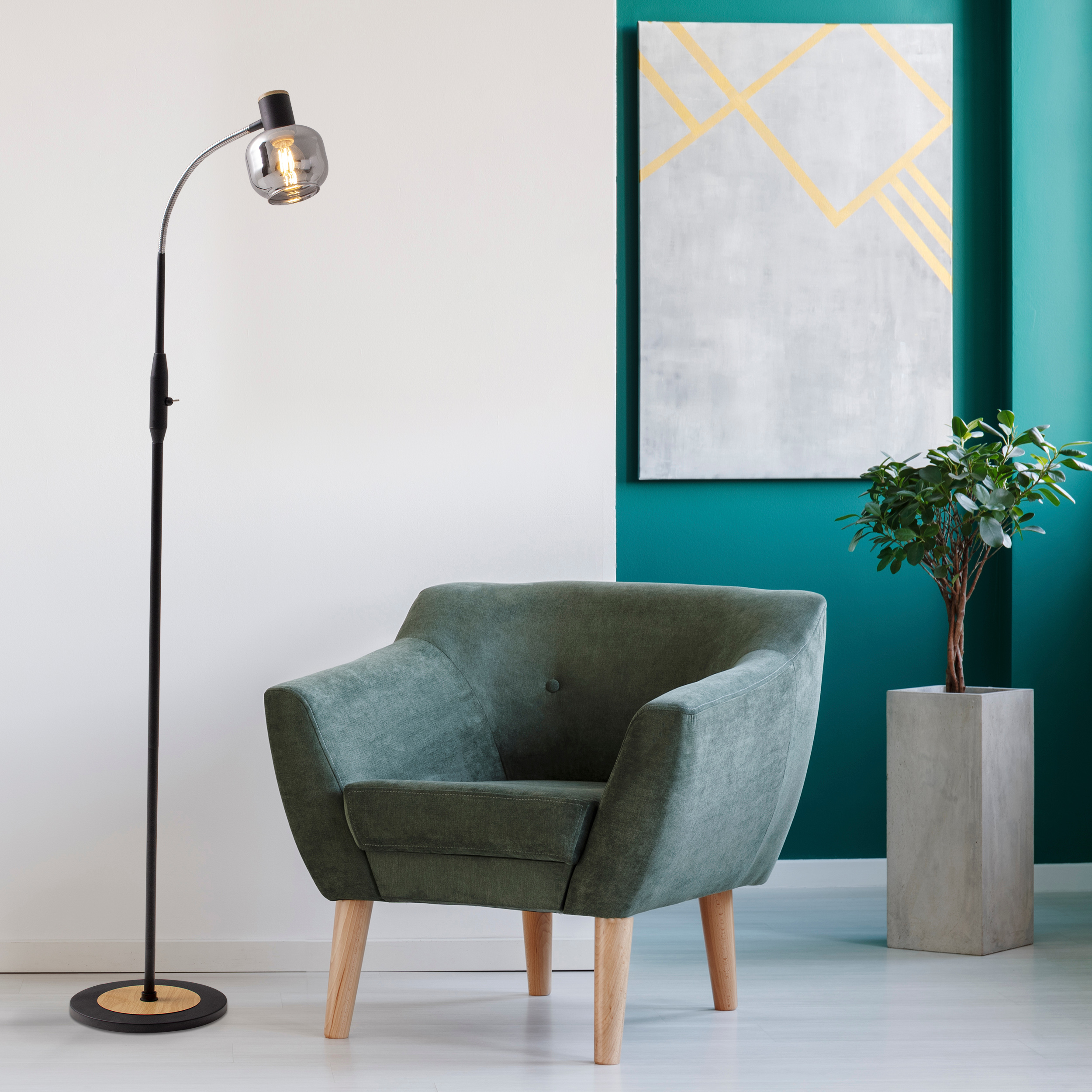 Eine schwarz-goldene Stehlampe neben einem grünen Sessel und einem Gemälde. Der Hintergrund ist weiß.