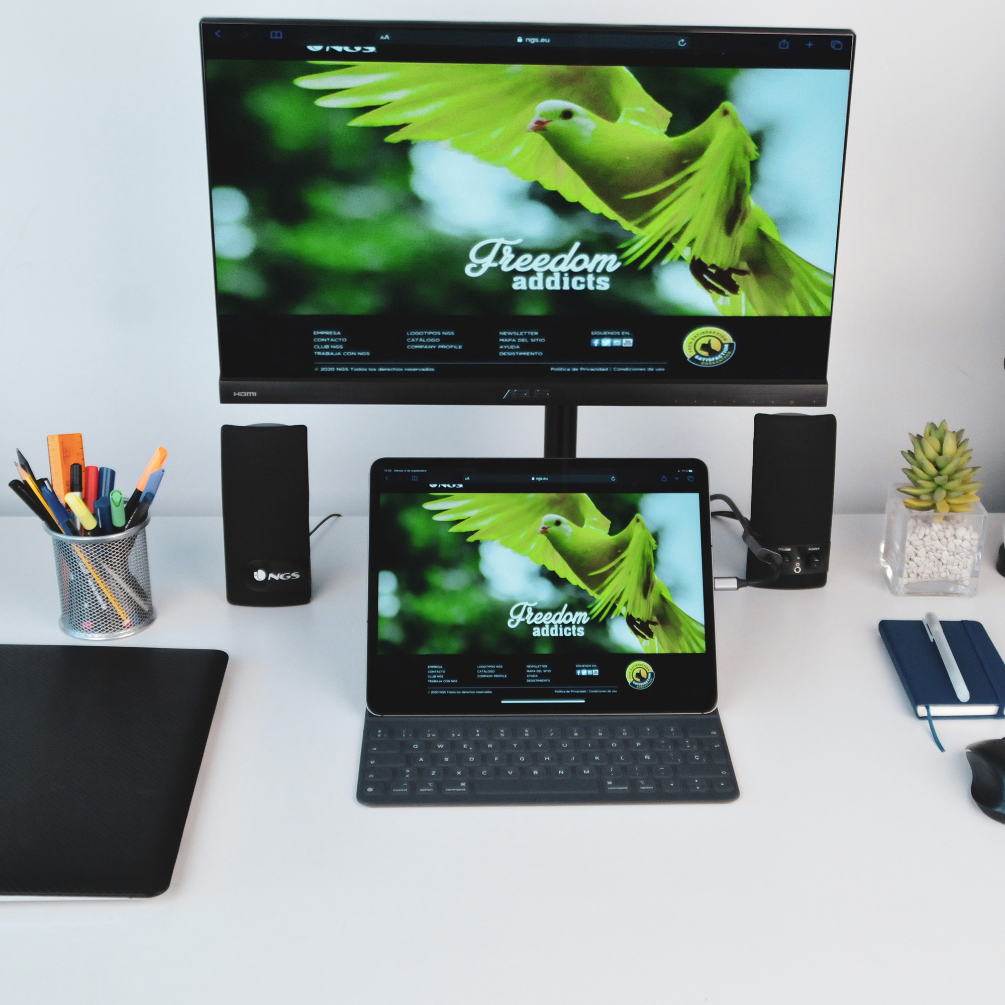 Una configuración de escritorio con monitor, altavoces, tableta y accesorios, mostrando un sitio web.
