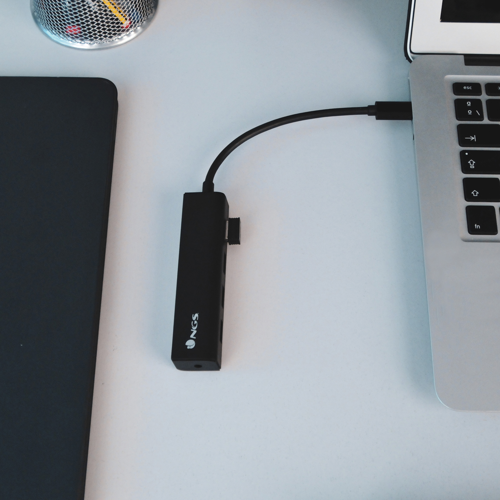 Concentrador USB negro conectado a una laptop. El hub tiene el logo NGS.