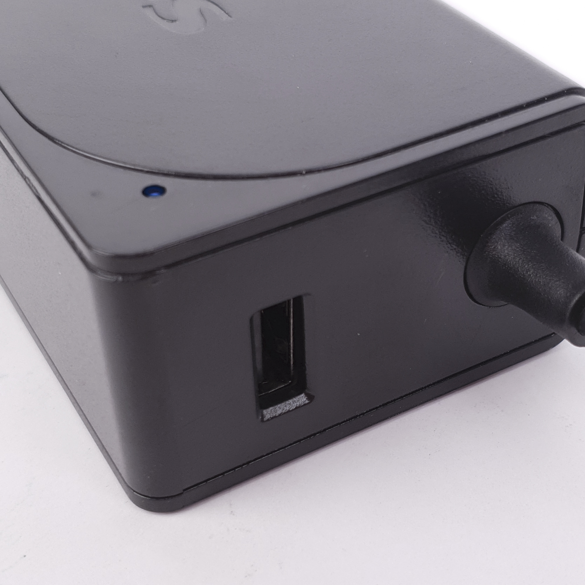 Una fuente de alimentación negra. El lado es visible, con un puerto USB. El logotipo está en la parte superior.