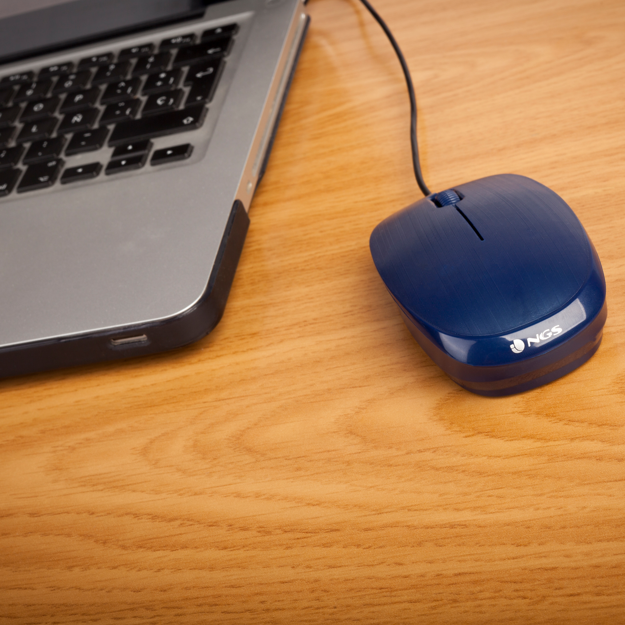 Un ordinateur portable et une souris d'ordinateur bleue sur un bureau en bois. La souris porte le logo NGS.