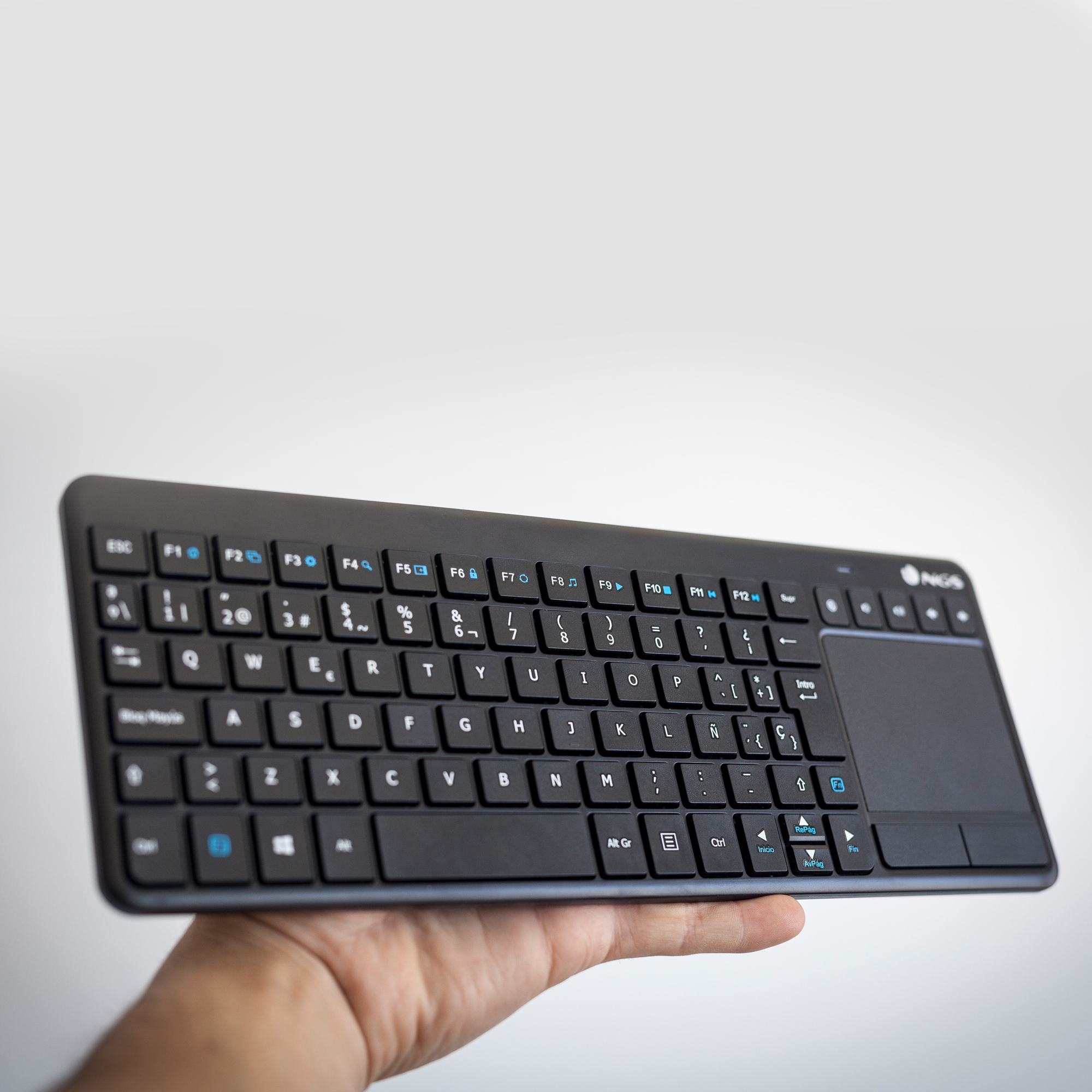 Una tastiera nera con touchpad, tenuta in mano. Tasti blu per funzioni speciali.