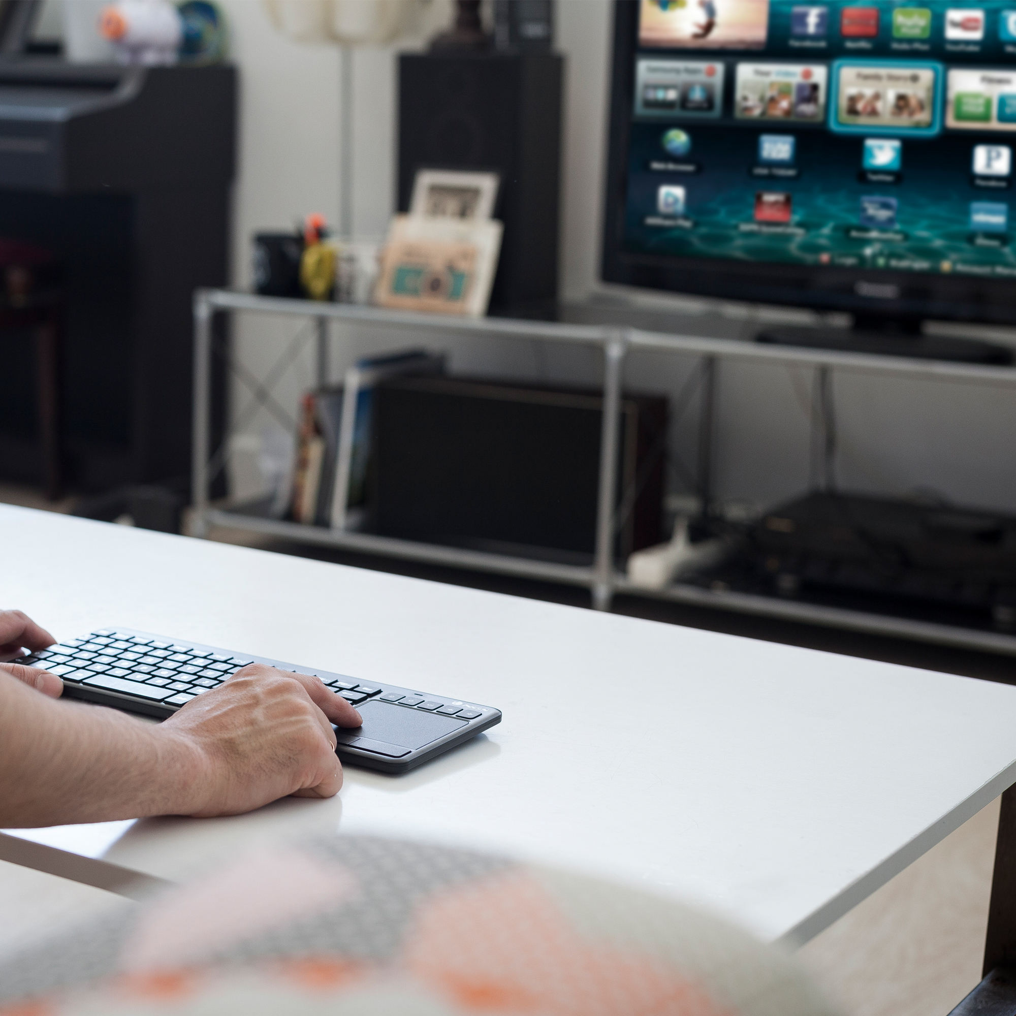 Una persona usa una tastiera su una scrivania bianca; una TV sullo sfondo.