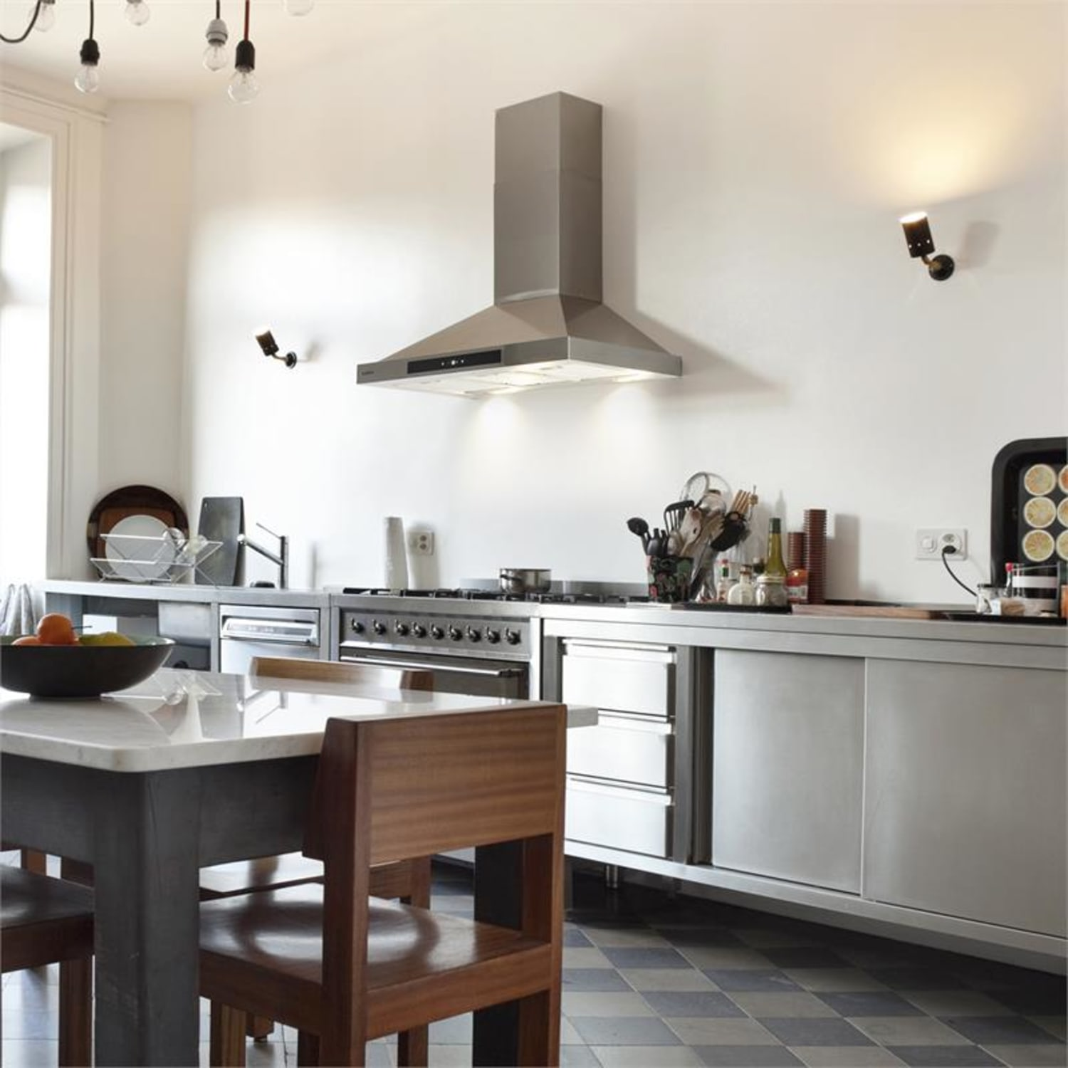 Moderne Küche mit Edelstahlgeräten, Tisch und Fliesenboden.