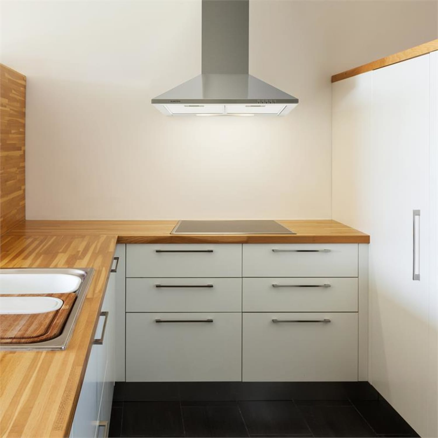 Cocina con gabinetes claros, encimera de madera, piso negro y campana extractora.