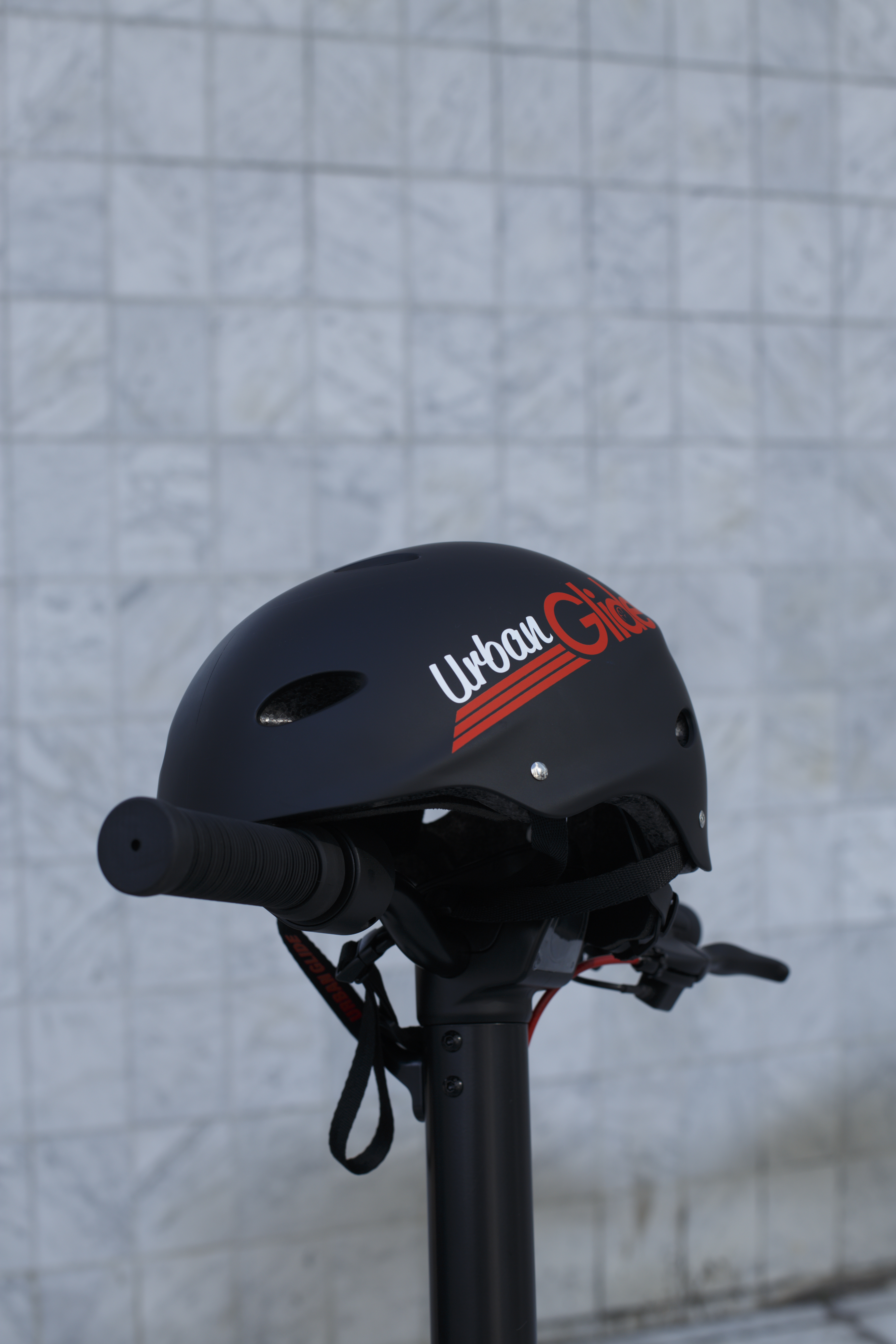 Casco Urban Glide negro sobre un manillar. El fondo es una pared de ladrillos blancos.