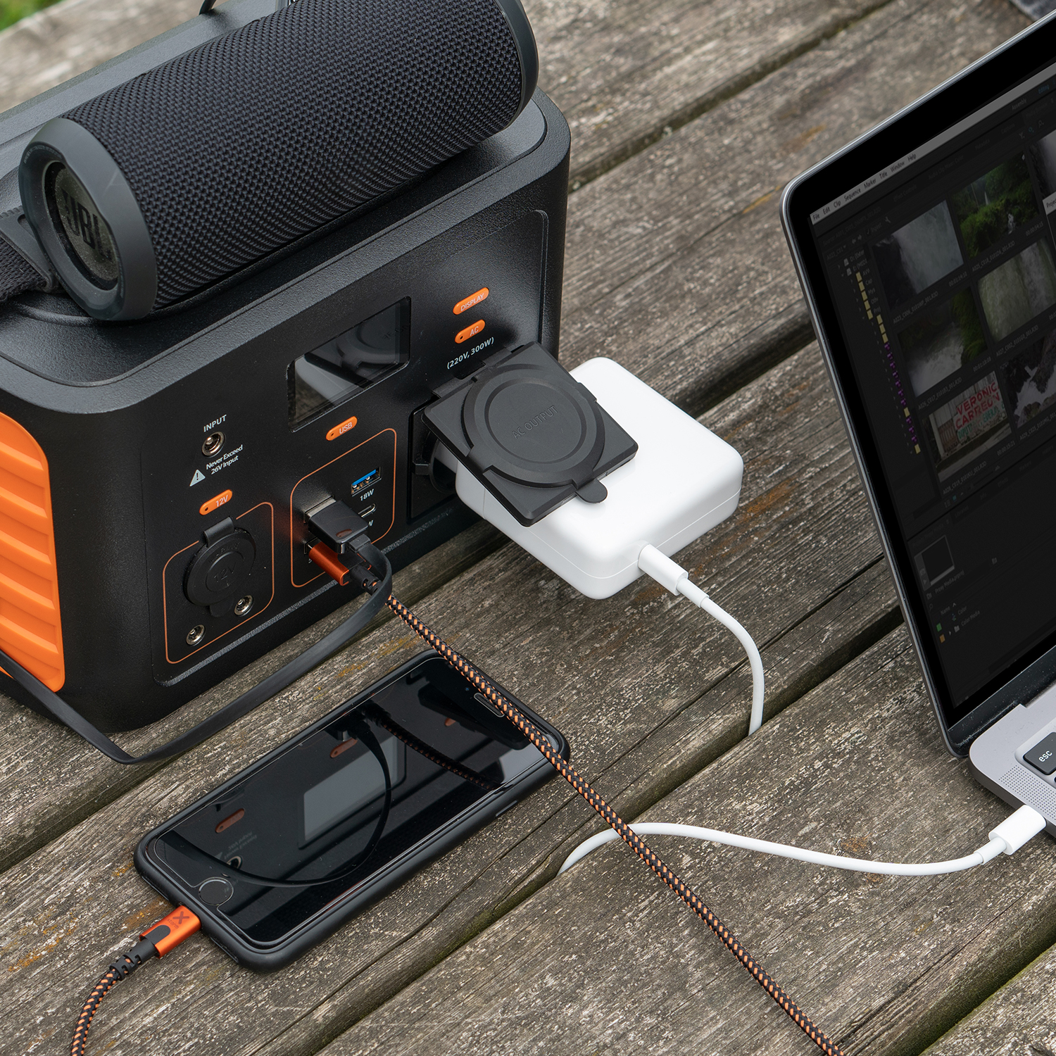 Szene im Freien mit Laptop, Telefon und Powerstation, alles mit Kabeln auf einem Holztisch verbunden.