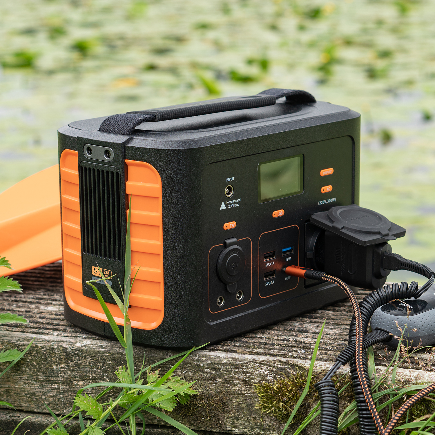 Schwarze und orange Powerstation auf Holz, mit Kabeln und Steckern. Grüner Hintergrund.