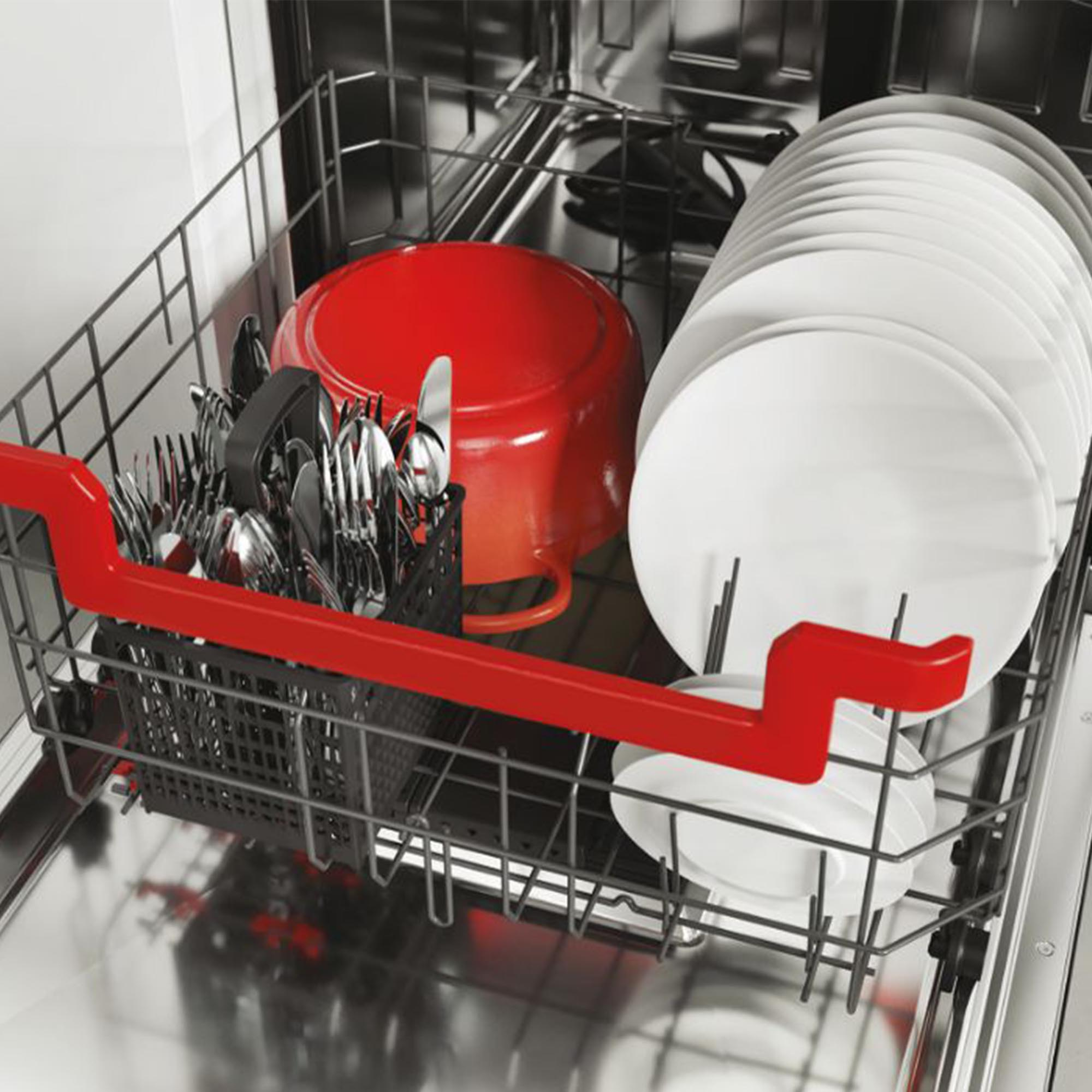 Interno della lavastoviglie con pentola rossa, piatti bianchi, posate e un manico rosso.