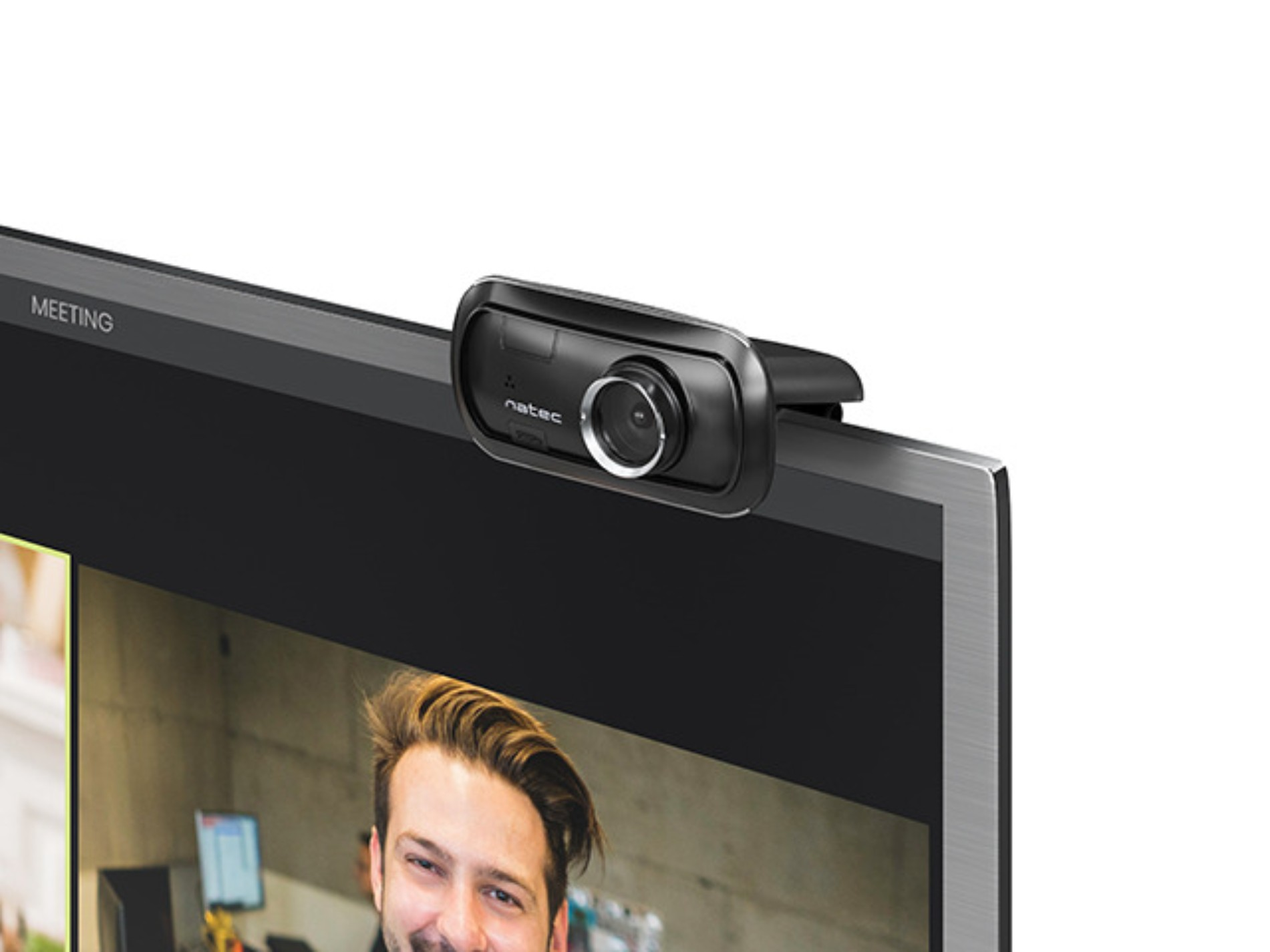 Kamera internetowa zamontowana na monitorze komputera. Osoba na ekranie, uśmiechnięta, w środowisku pracy.