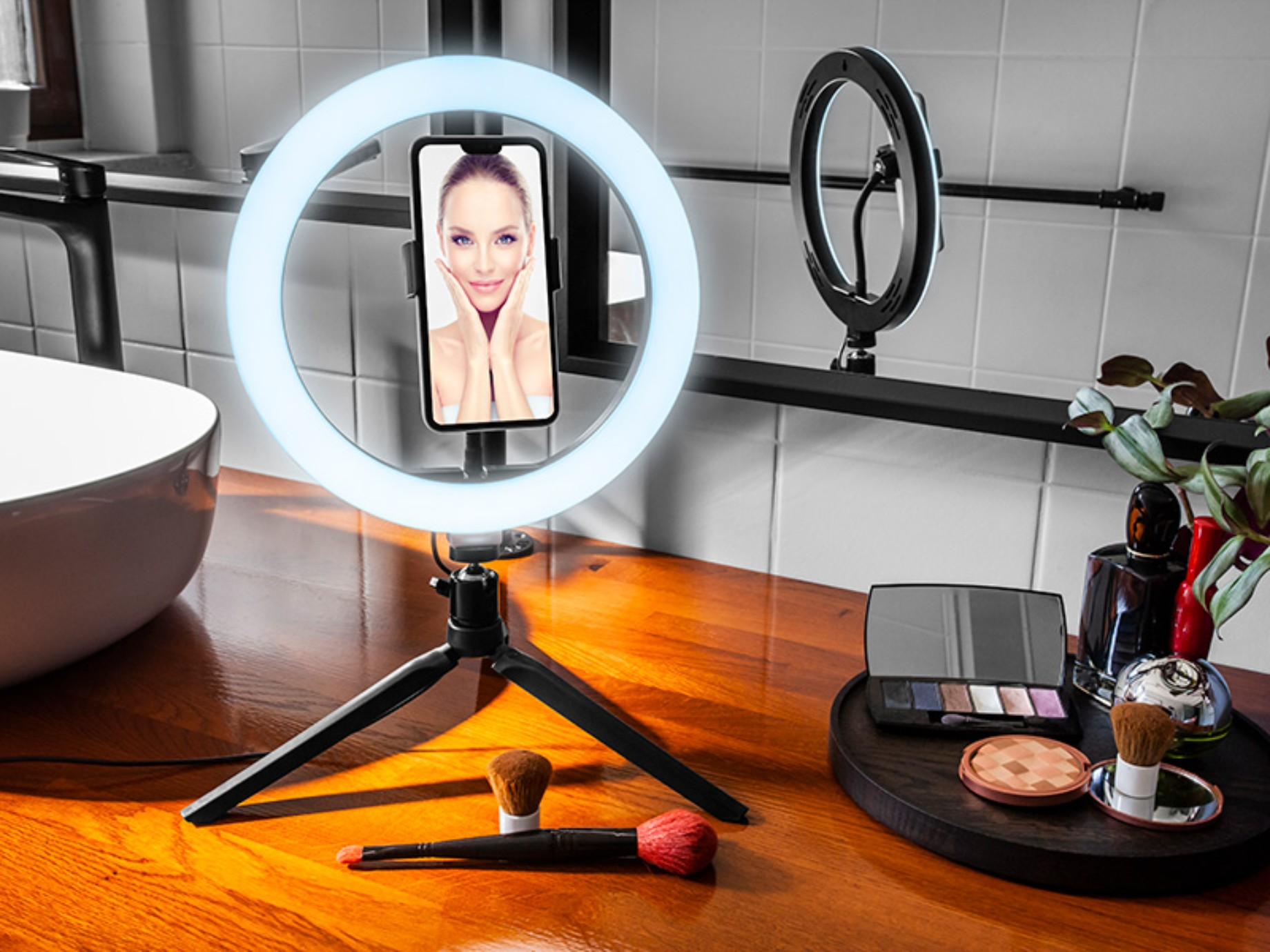 Ein Make-up-Setup mit Ringlicht, Telefon und Make-up. Auf dem Telefonbildschirm ist ein Frauen Gesicht zu sehen.