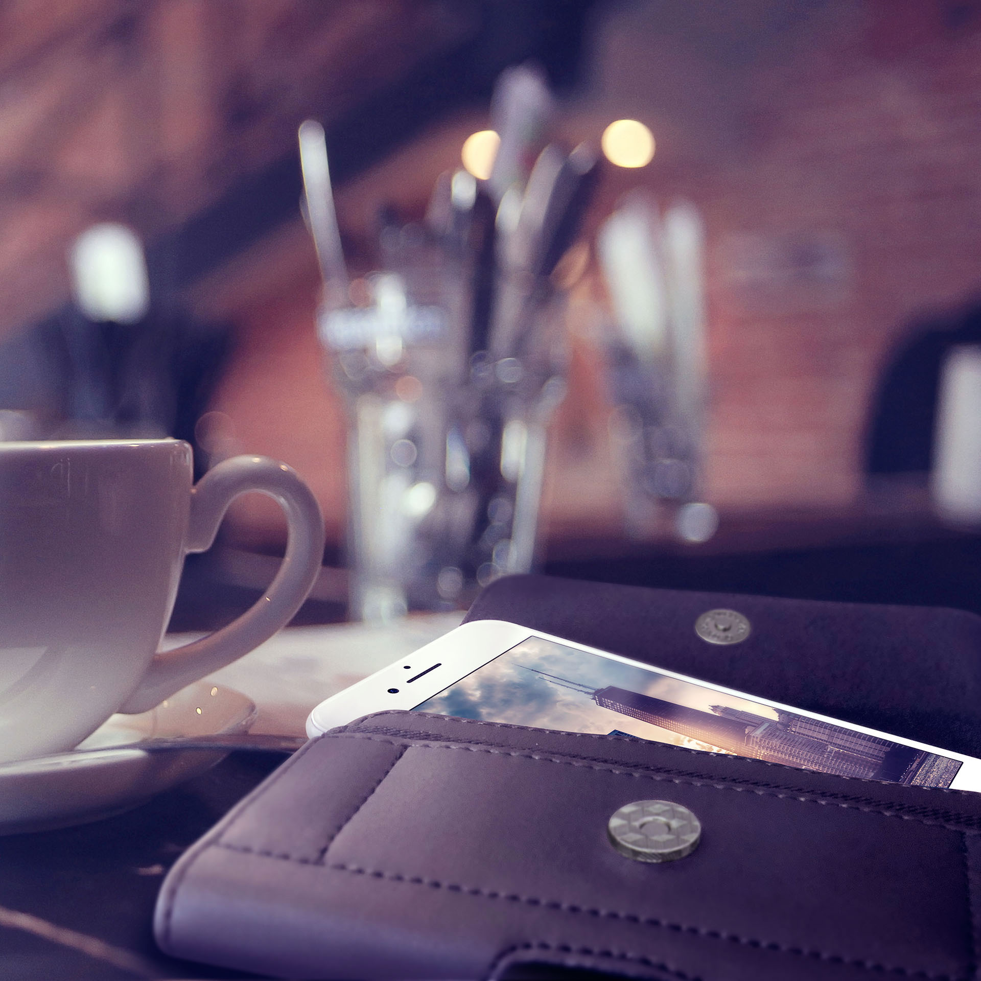 Kaffeetasse und Telefon in dunkler brauner Hülle auf einem Cafétisch. Hintergrund unscharf.