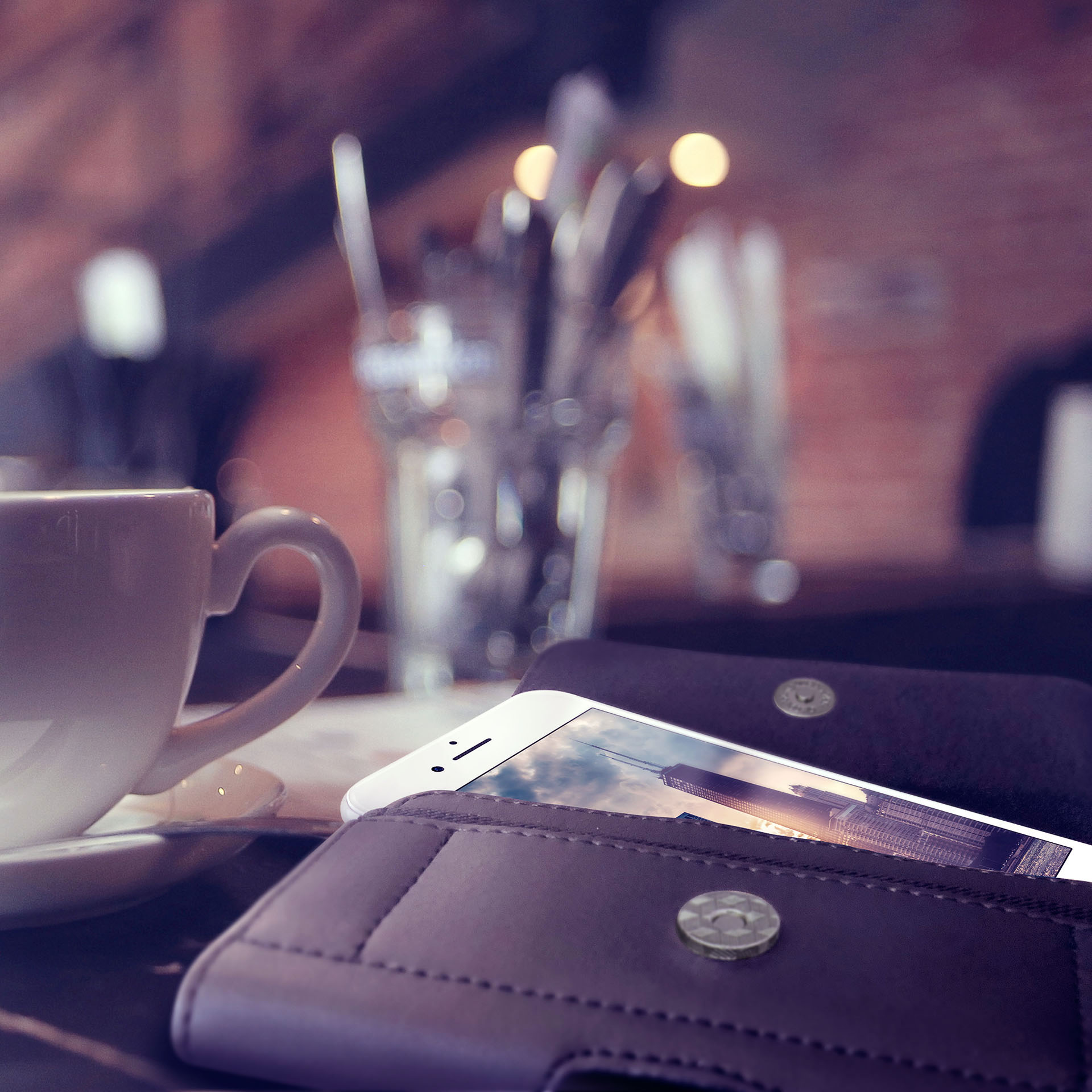 Ein Telefon in einer braunen Ledergeldbörse mit einer weißen Tasse und Besteck auf einem Tisch, verschwommener Hintergrund mit Lichtern.