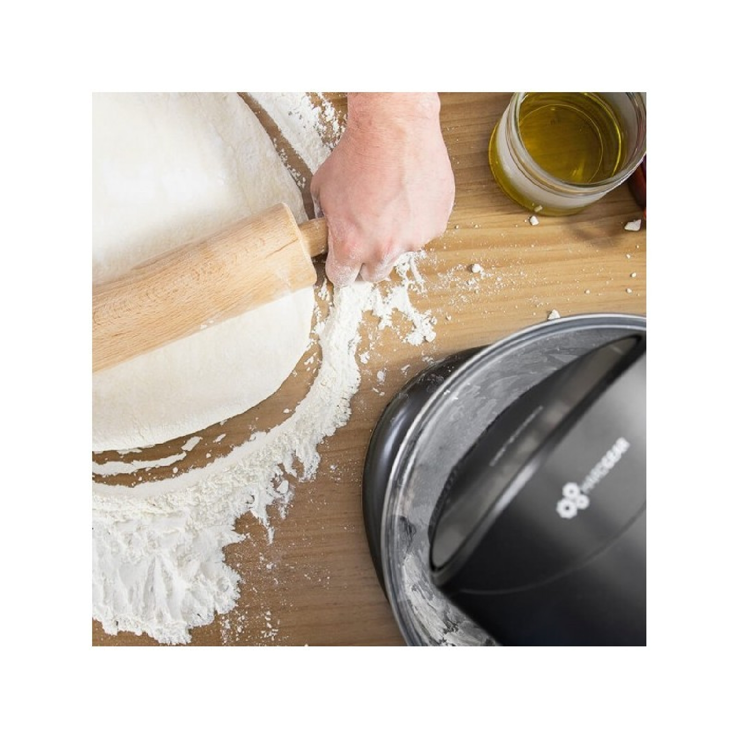 Manos extendiendo masa con rodillo sobre superficie de madera con harina y bandeja de pizza.