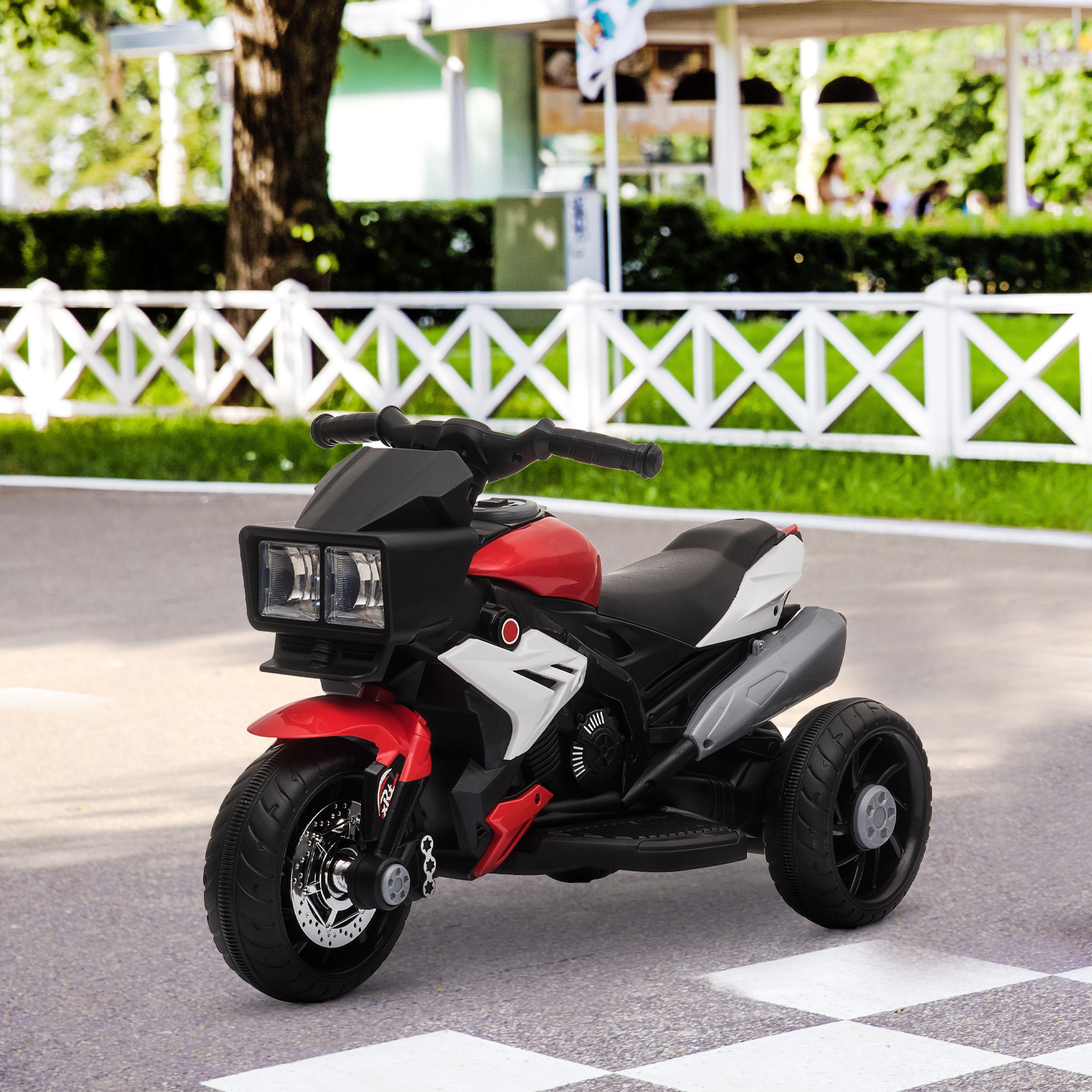 Una moto giocattolo rossa e nera su una strada con una recinzione bianca sullo sfondo.