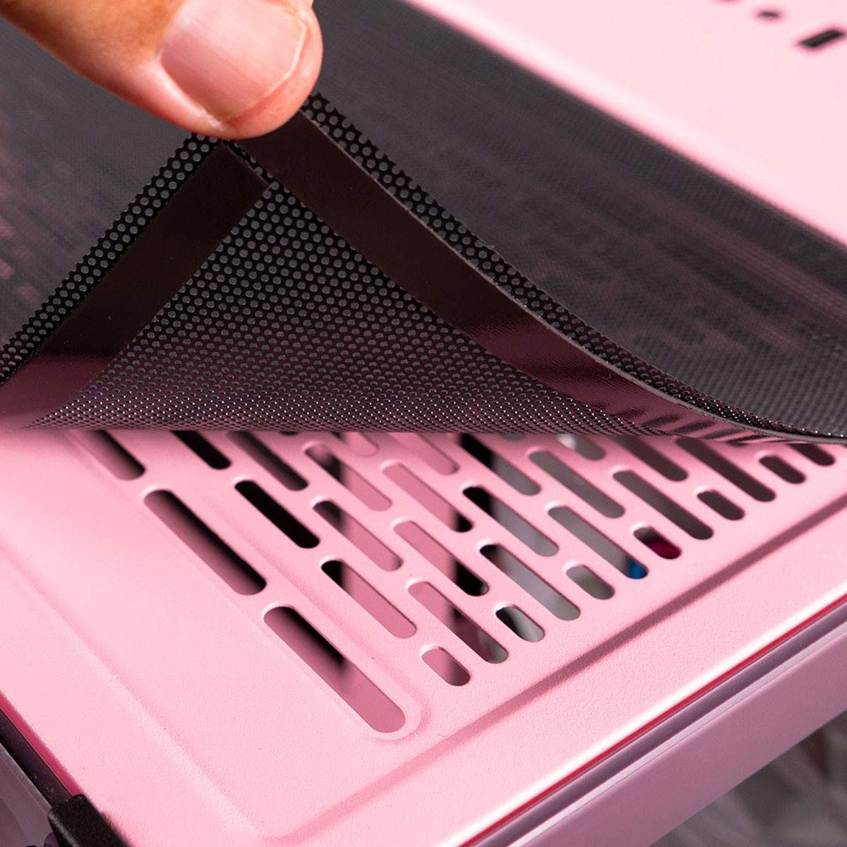Una mano despegando una malla negra punteada de una carcasa de computadora rosa, primer plano.