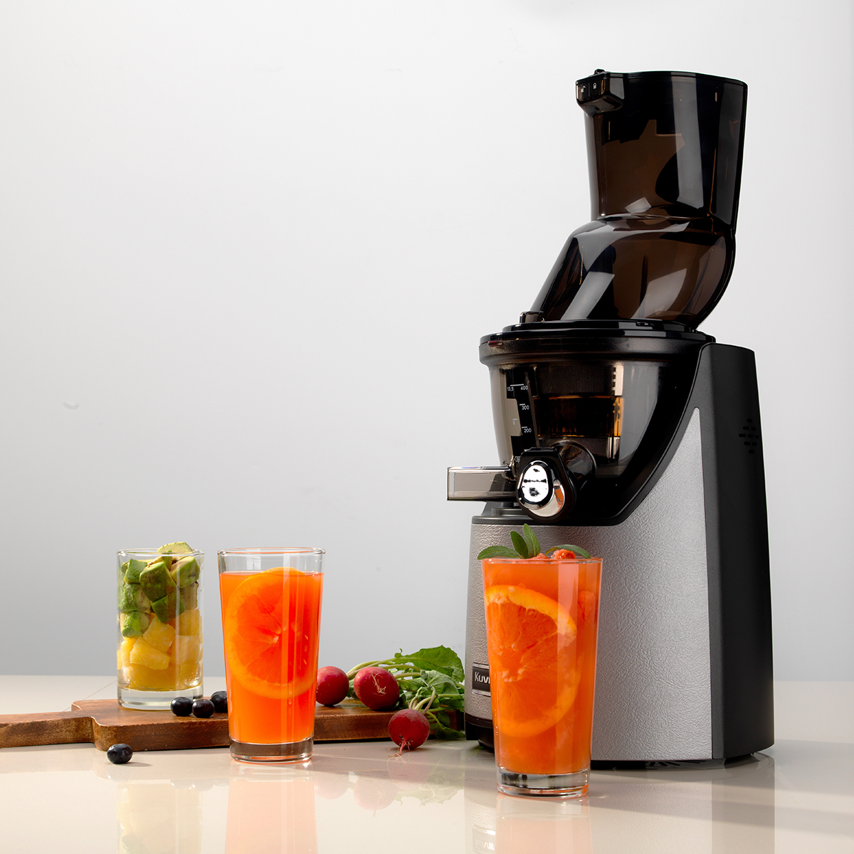 Exprimidor con vasos de zumo. Un vaso con rodajas de naranja, uno con kiwi y otro con zumo y fresas.
