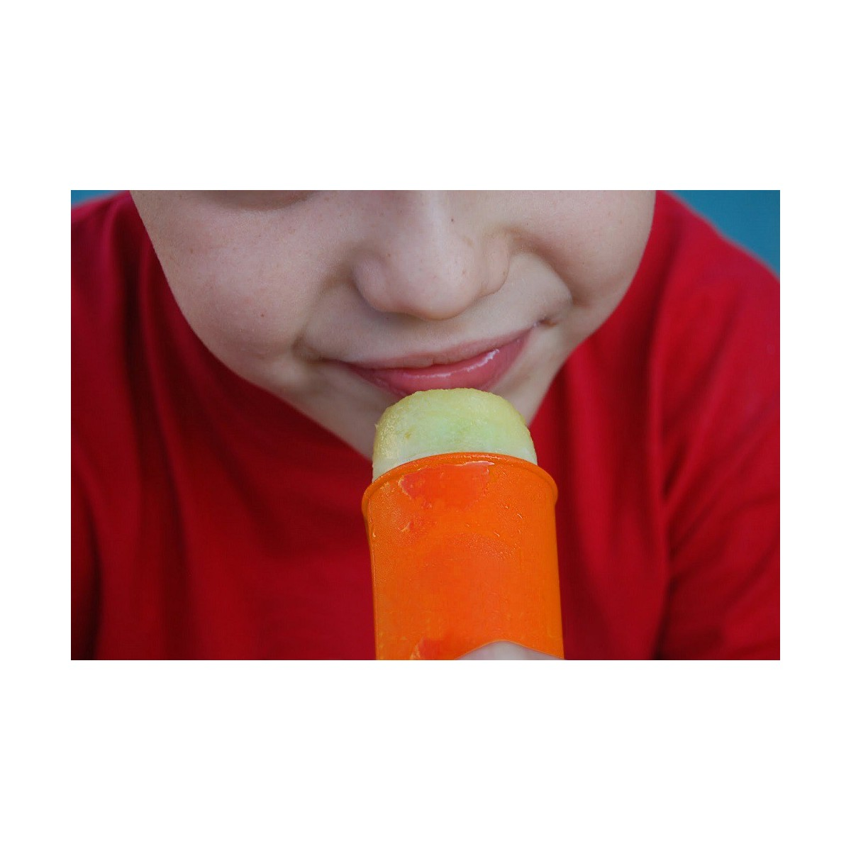 Un niño comiendo un helado. El helado es naranja con un centro verde. Se ve la cara del niño.
