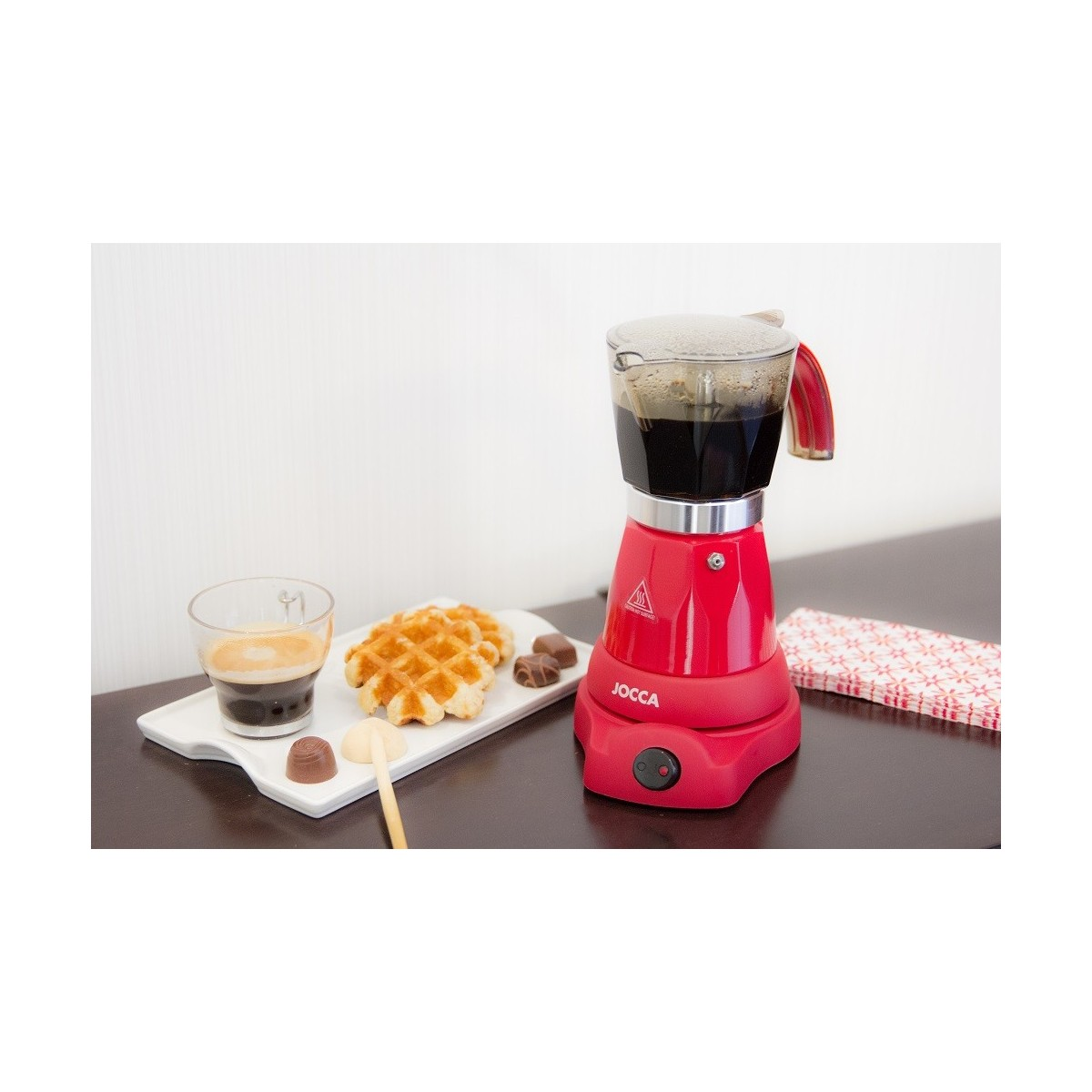 Caffettiera rossa con caffè, waffle e cioccolatini su un tavolo.